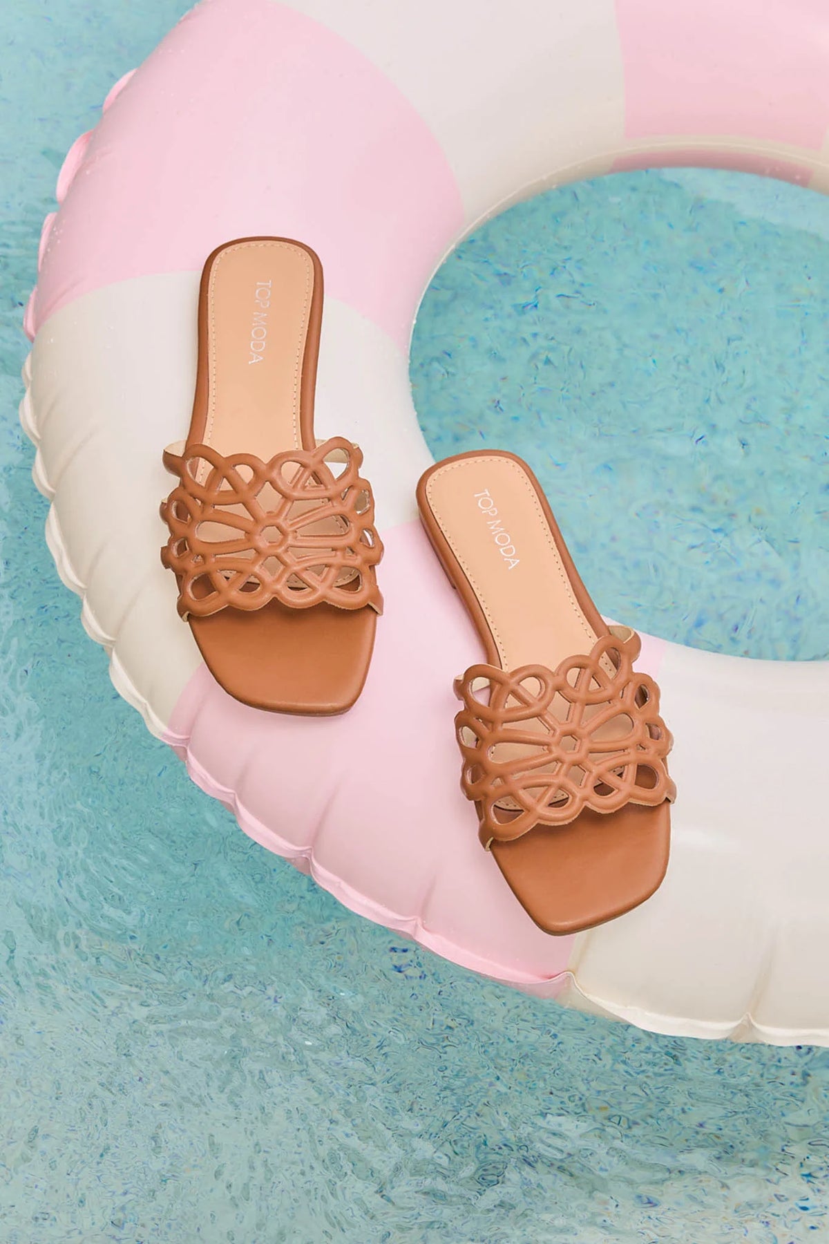 Brown floral cutout slide sandals styled on pink pool float over blue water - Resort Look | Avara