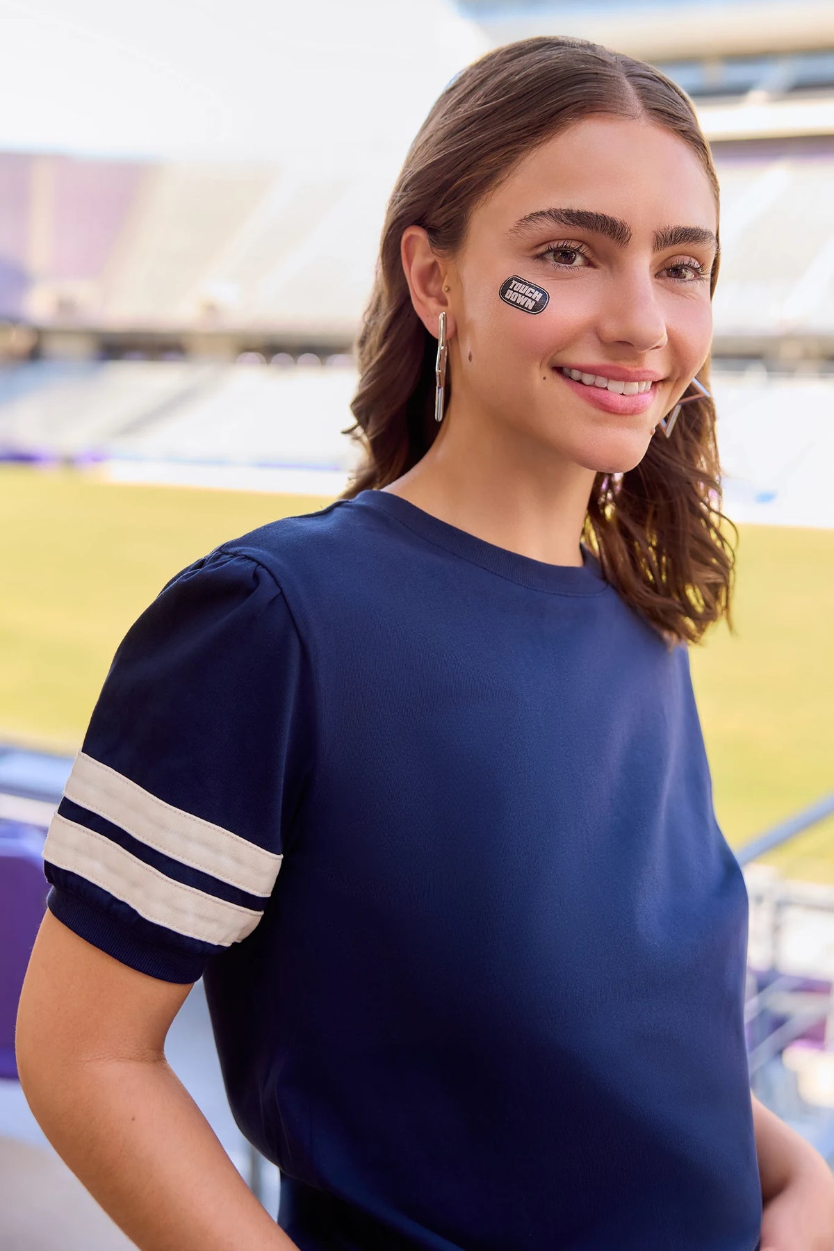 Alice Navy Striped Sleeve Tee close-up, varsity stripe detail on puff sleeve, stadium lifestyle shot | Avara