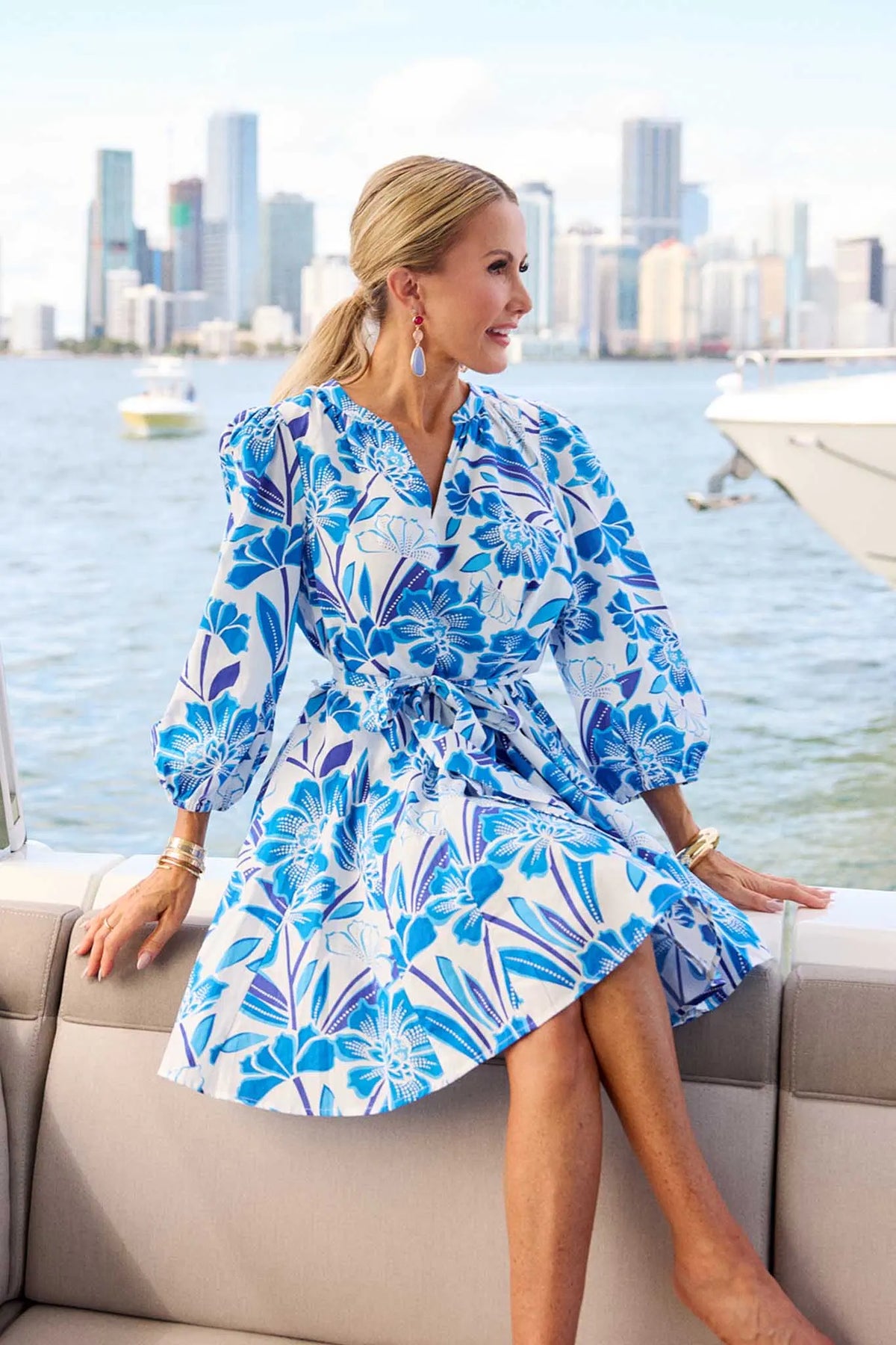 Woman in blue floral mini dress seated on boat with city skyline - Vacation Styled Look | Avara