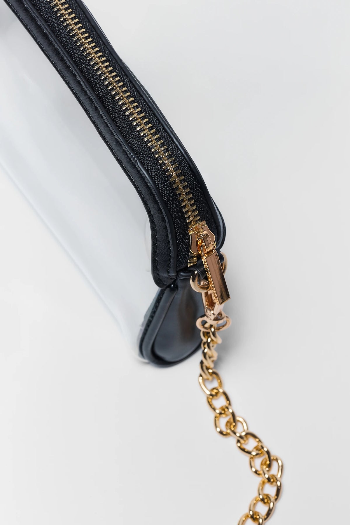 Clear crossbody bag gold zipper and black trim hardware detail with chain strap attachment | Avara
