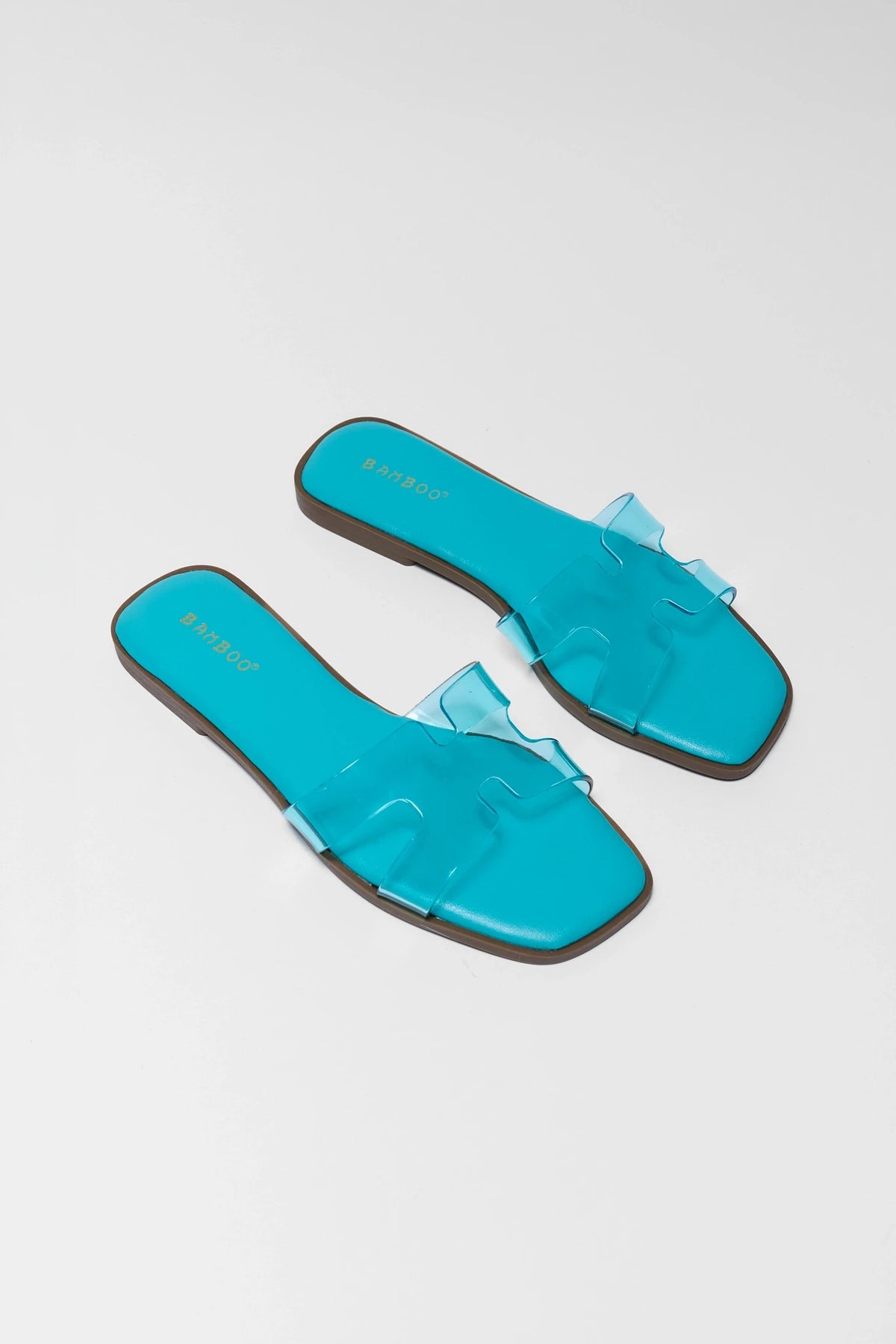 Turquoise blue jelly slip-on sandals pair angled overhead, clear straps with teal footbed detail | Avara
