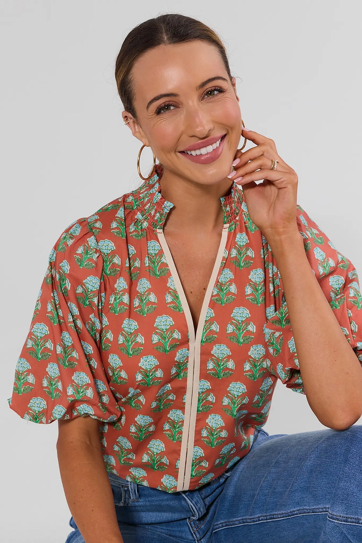 THML orange floral block print puff sleeve top with cream V-neckline trim, seated on-model with jeans | Avara