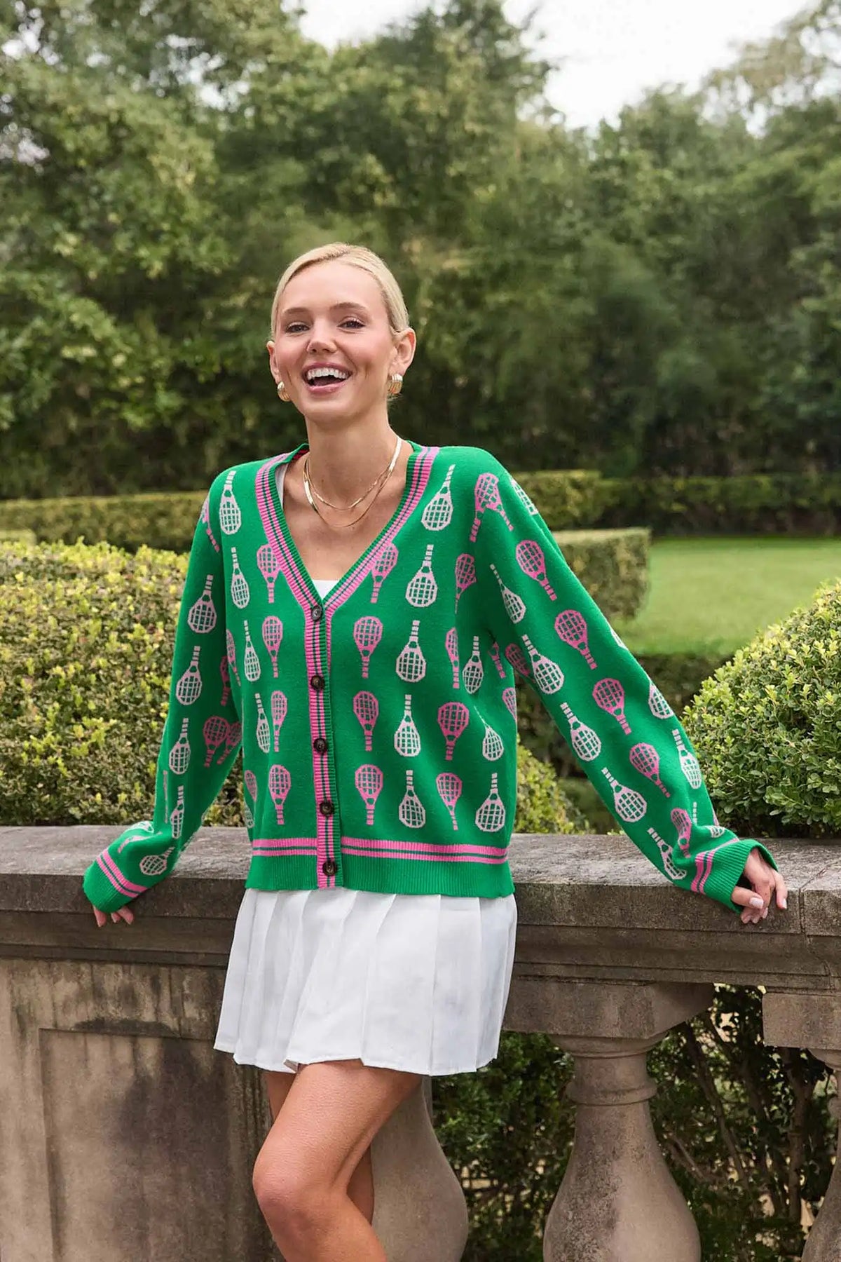 Green racket print cardigan styled over white skirt, outdoor lifestyle shot | Avara