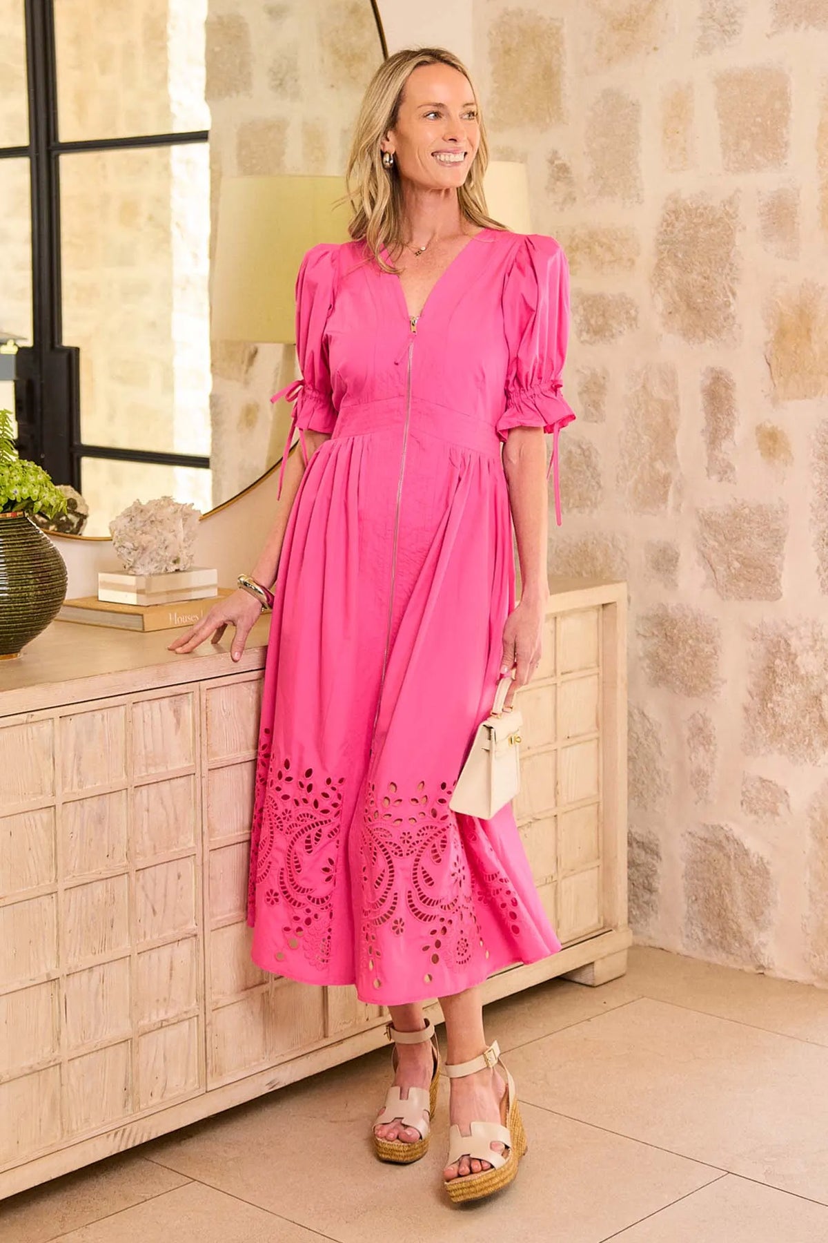 Woman in a pink dress standing in a room with stone walls and a wooden cabinet.