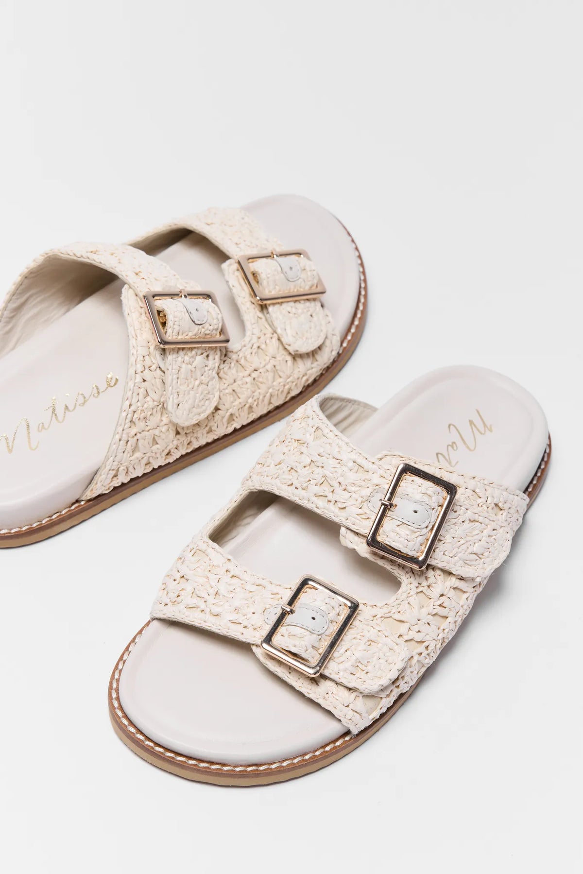 Tan woven raffia sandals with double gold buckles, close-up overhead angle | Avara