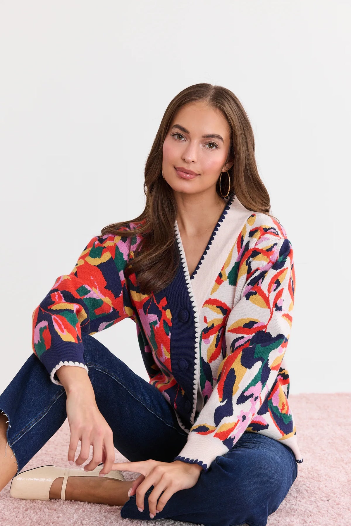 Leslie Navy Floral Cardigan seated lifestyle shot, colorful patterned knit with scalloped edges paired with dark jeans and nude flats | Avara
