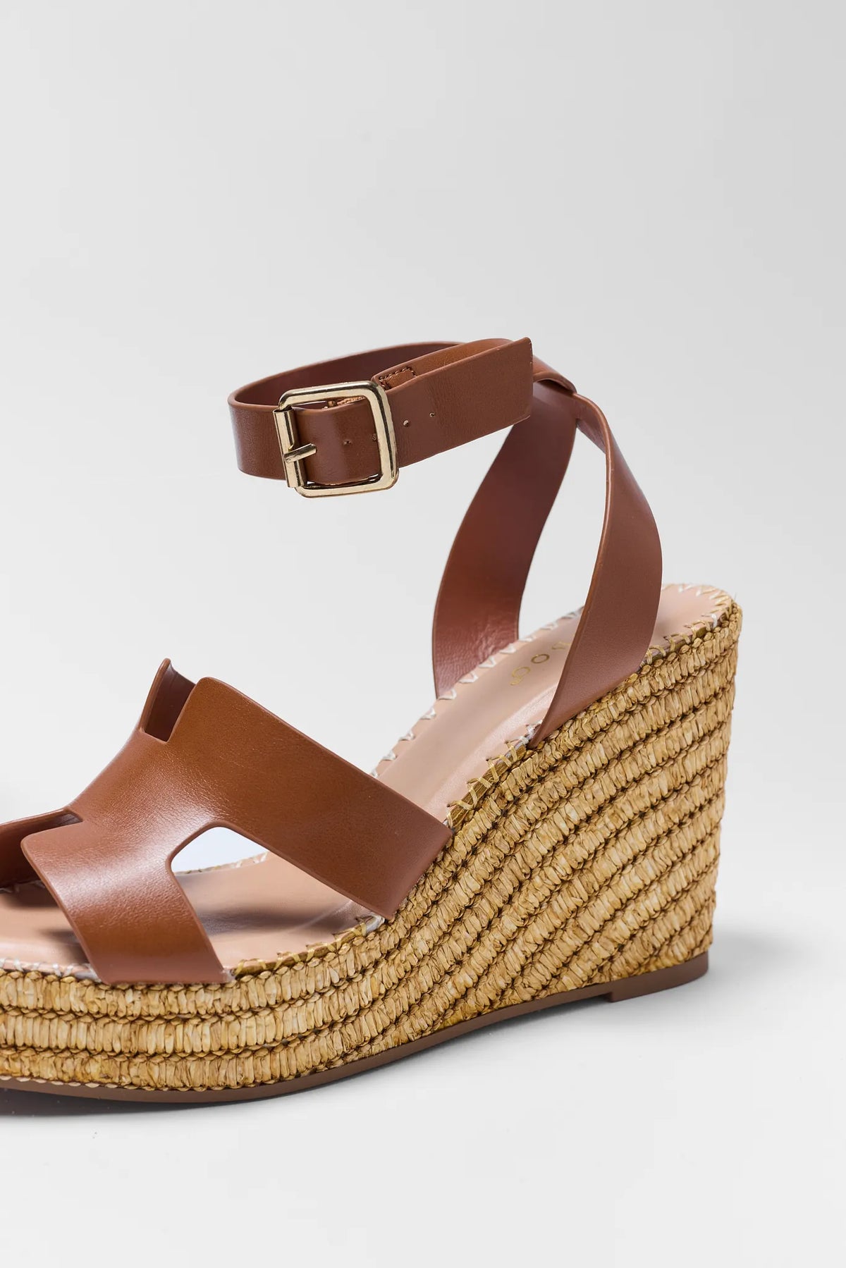 Brown leather wedge sandal close-up showing H-strap toe band, gold buckle ankle strap, and raffia platform | Avara