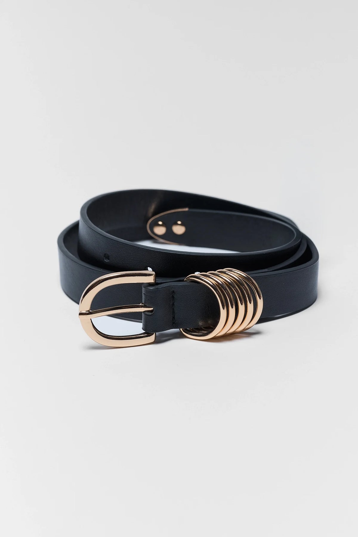 Marley Black Faux Leather Belt coiled with gold oval buckle and multi-ring hardware detail - Flat Lay | Avara