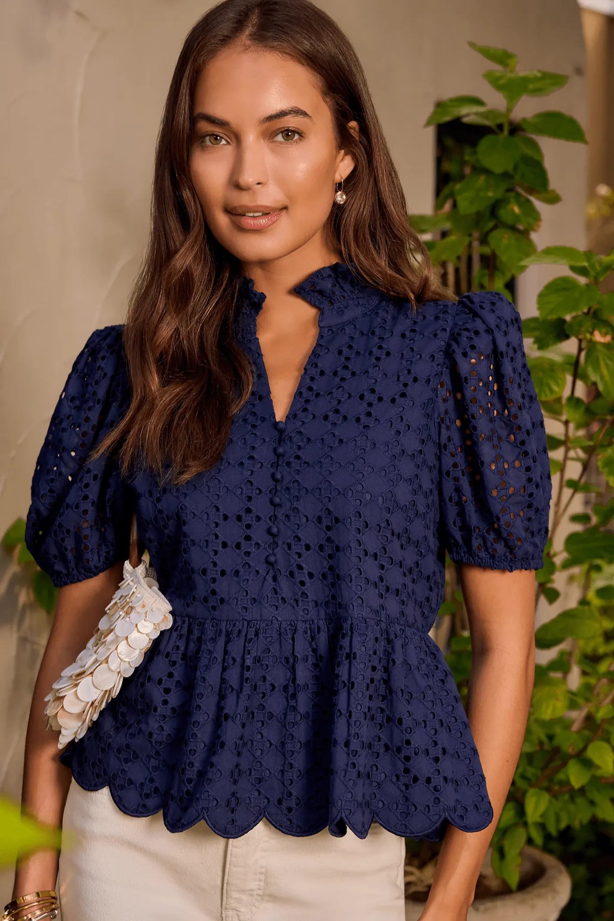 Navy eyelet peplum top in lifestyle setting with greenery, showing scalloped hem and puff sleeves | Avara