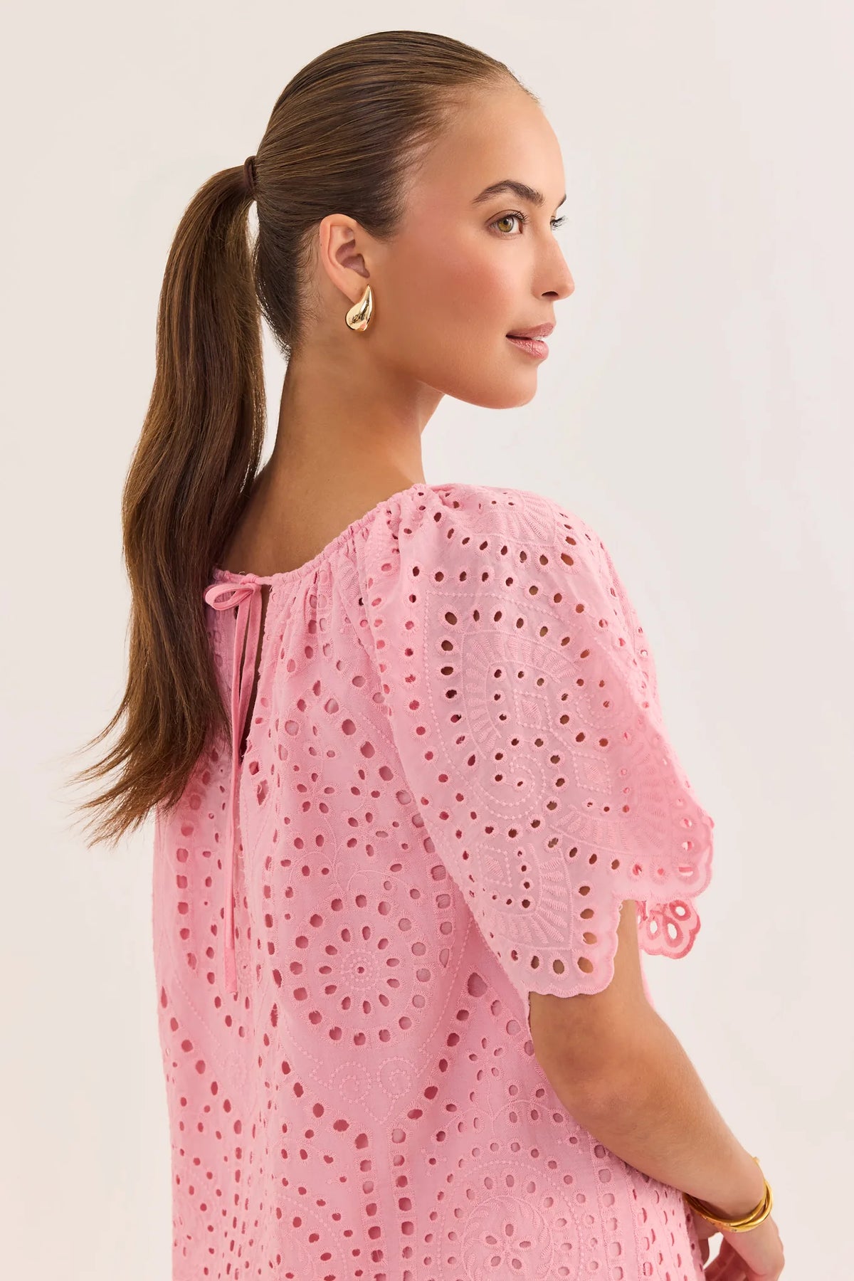 Pink eyelet tunic dress back view showing tie neckline detail and scalloped flutter sleeves | Avara
