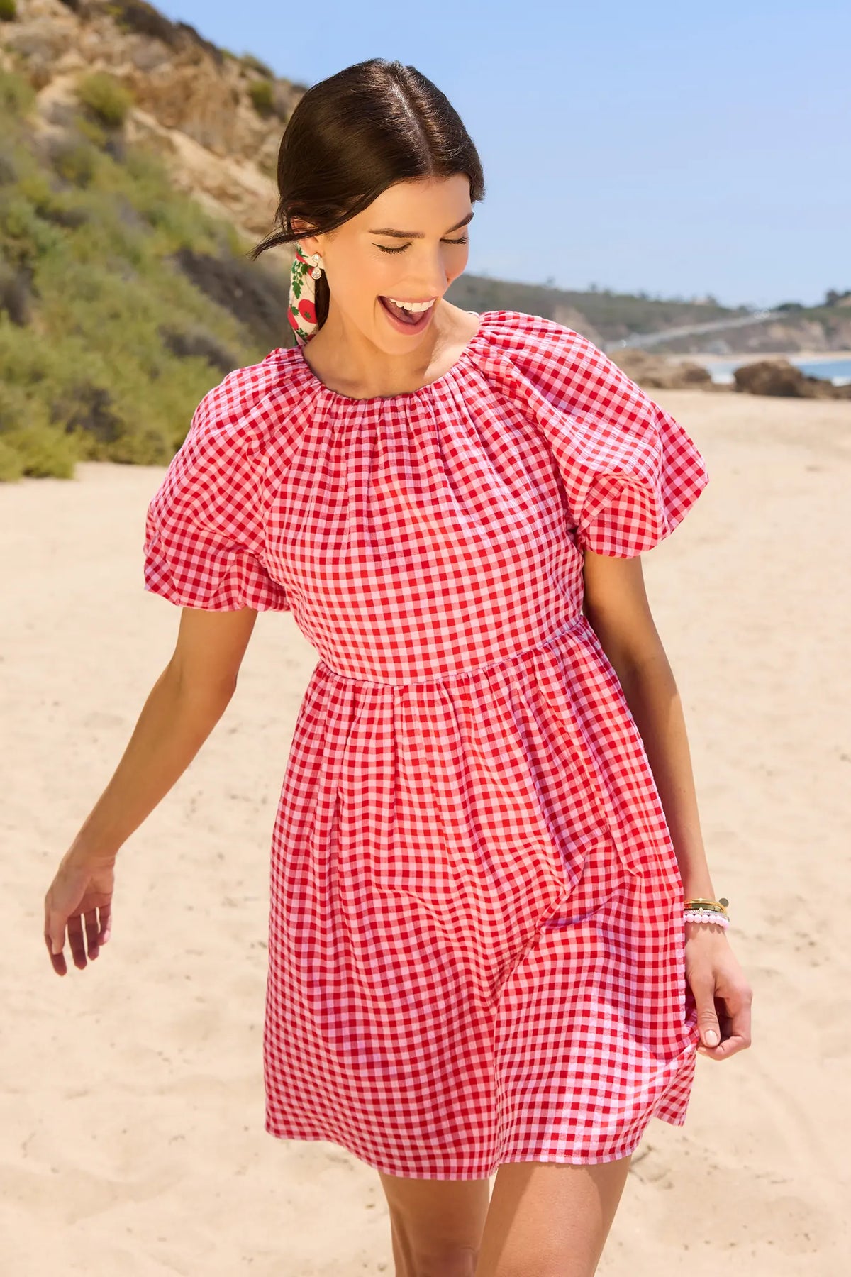 Red gingham short dress with puff sleeves worn on beach, summer lifestyle shot | Avara