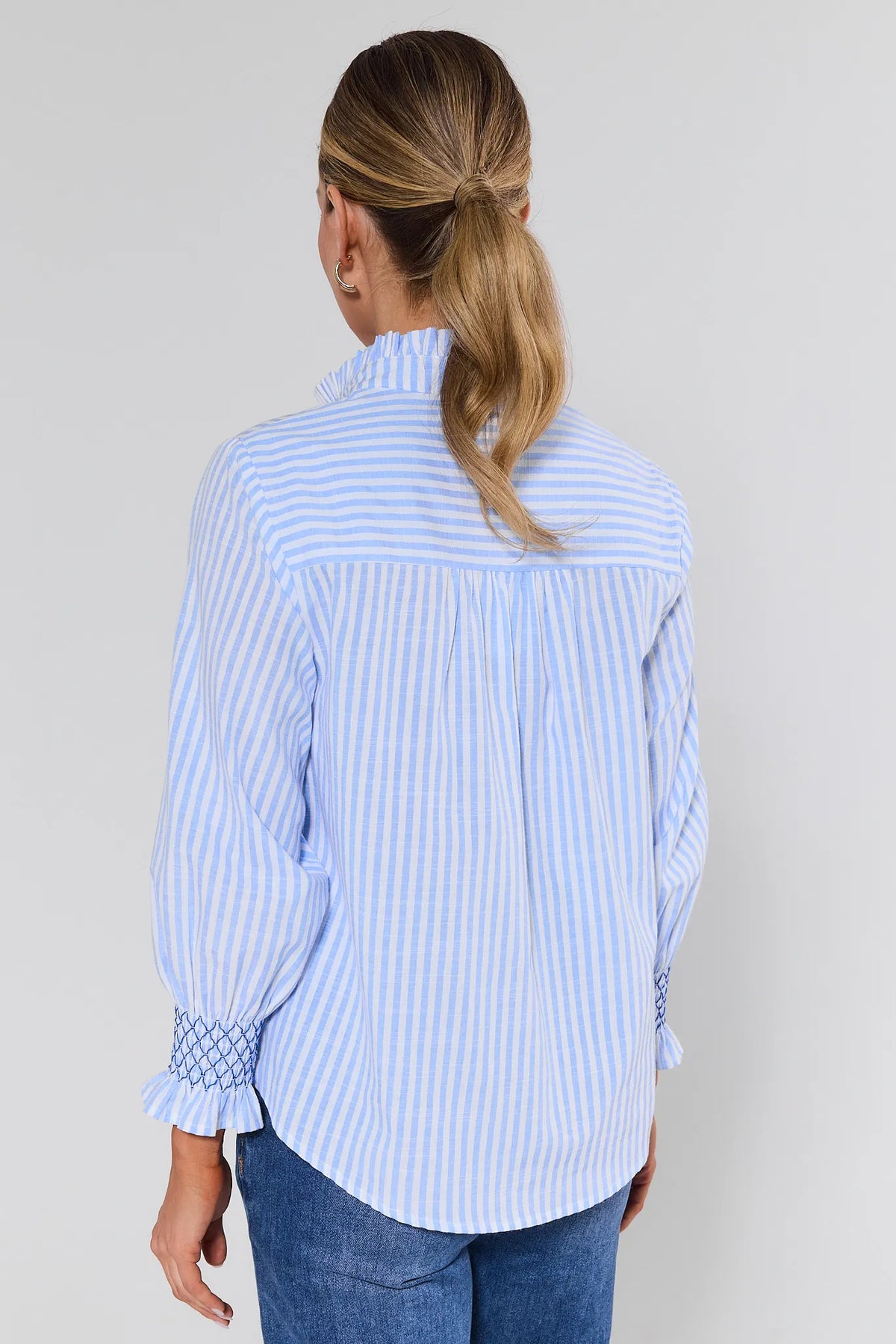 Woman wearing a light blue and white striped shirt against a plain background