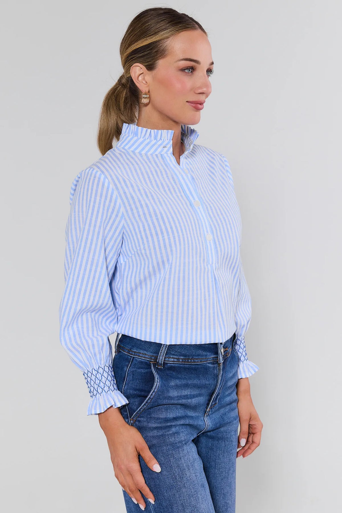 Woman wearing a blue and white striped shirt and jeans against a plain background