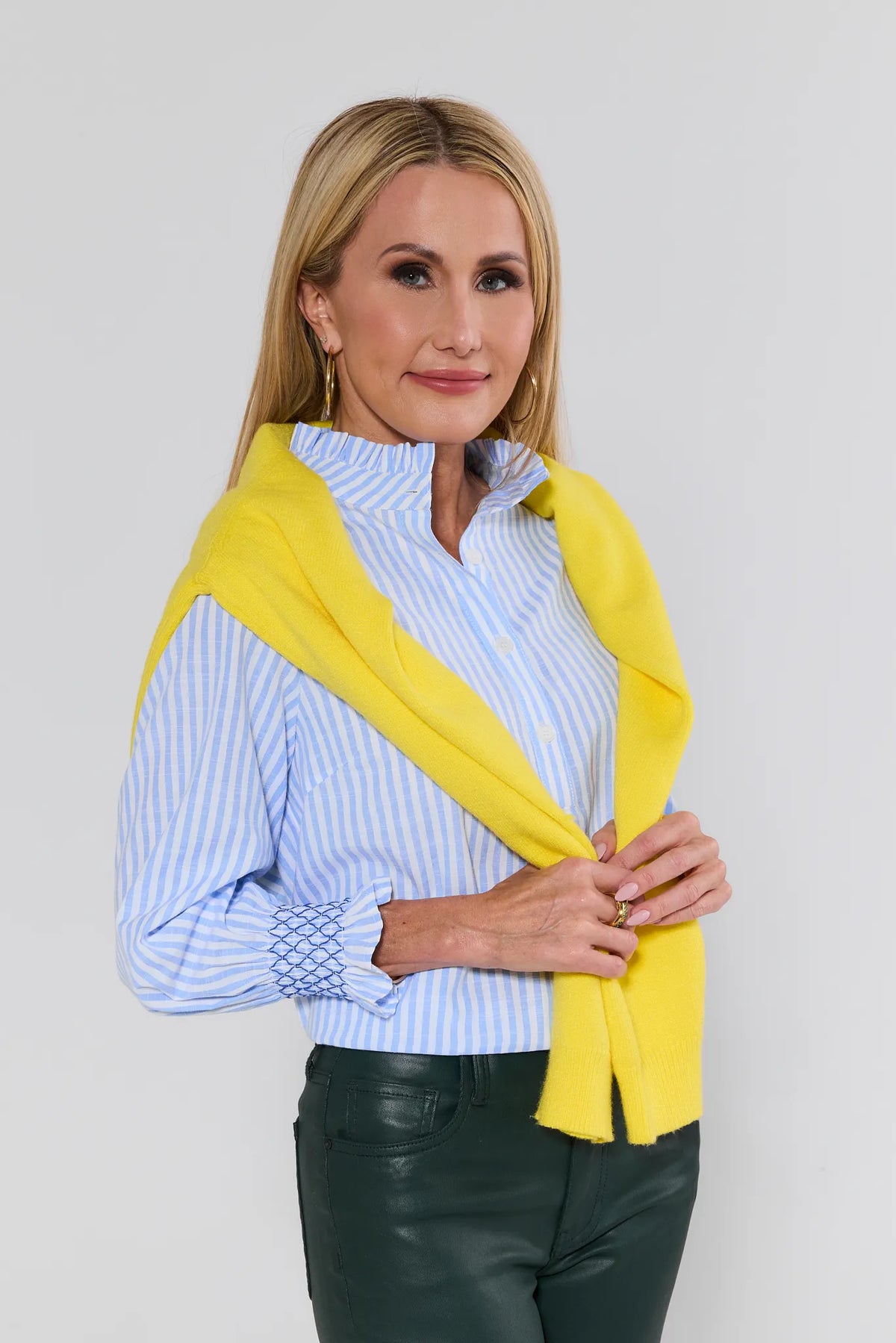 Woman wearing a yellow sweater over a blue and white striped shirt on a plain background