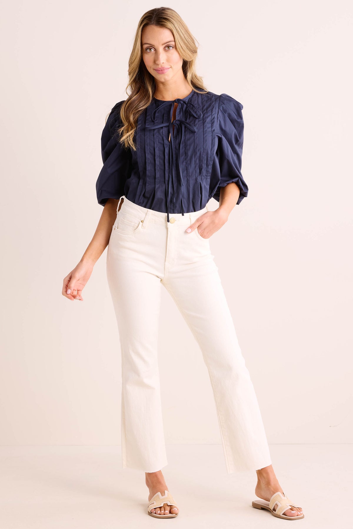 Woman wearing Kelsey Ecru Kick Flare Jeans full-length front view, styled with navy blouse and beige sandals | Avara