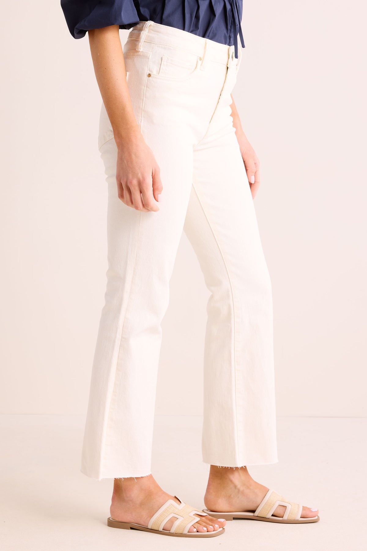 Kelsey Ecru Kick Flare Jeans side view showing raw hem and flare silhouette, paired with woven slide sandals | Avara