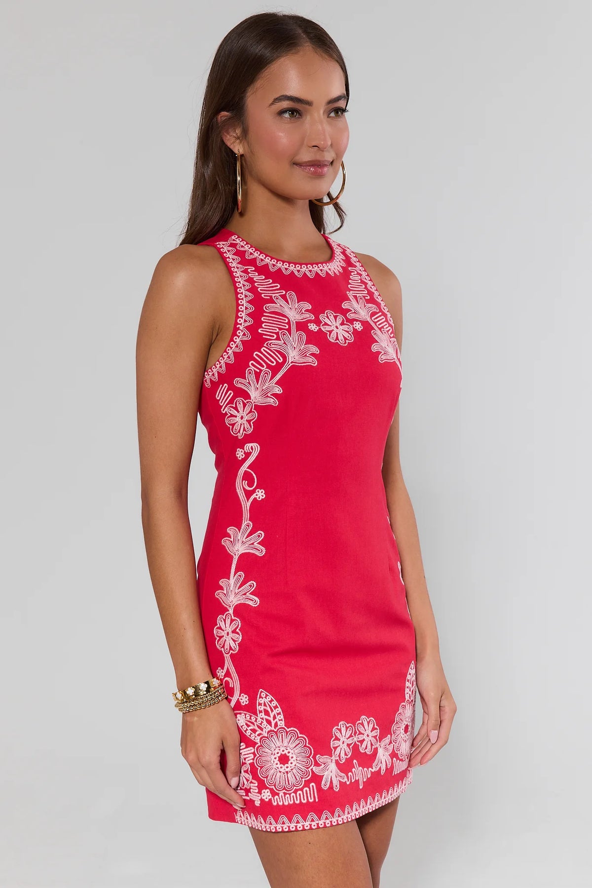 side shot Woman wearing a red dress with white floral embroidery on a plain background