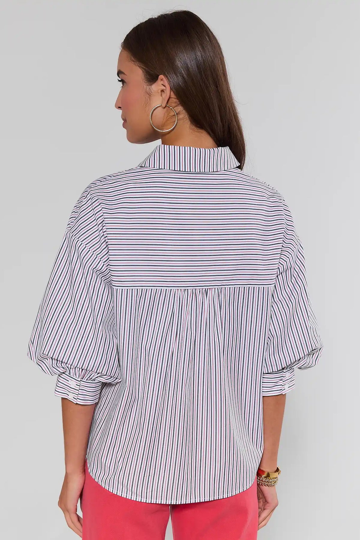 Woman standing wearing a striped shirt and pink pants on a plain background