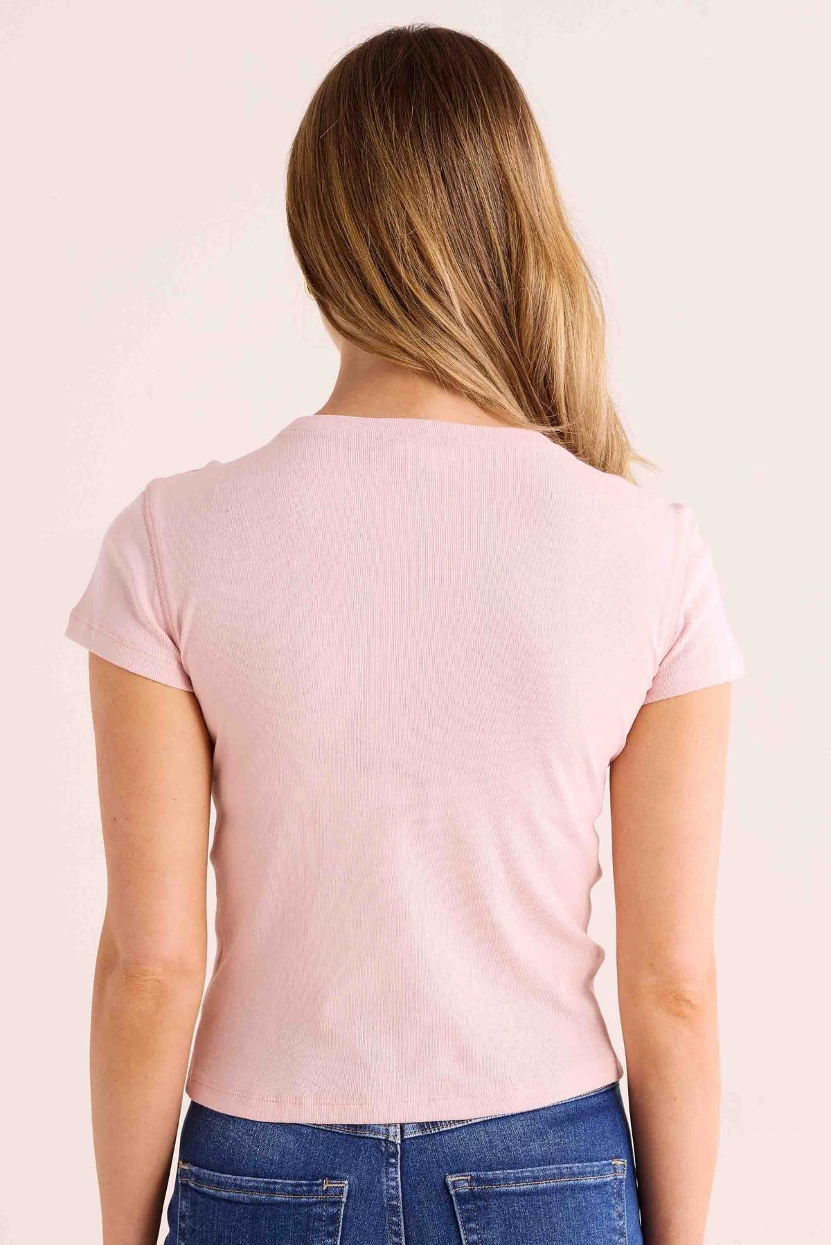 Back view of Aria Pink Fitted Tee, baby pink ribbed fabric, short sleeves, fitted silhouette, styled with blue denim | Avara