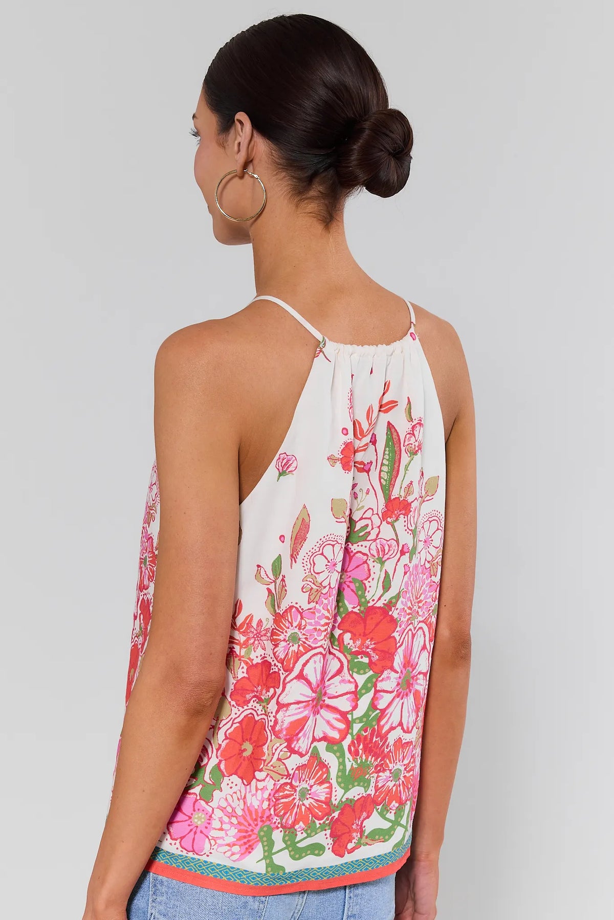 Woman standing wearing a floral sleeveless top against a plain background