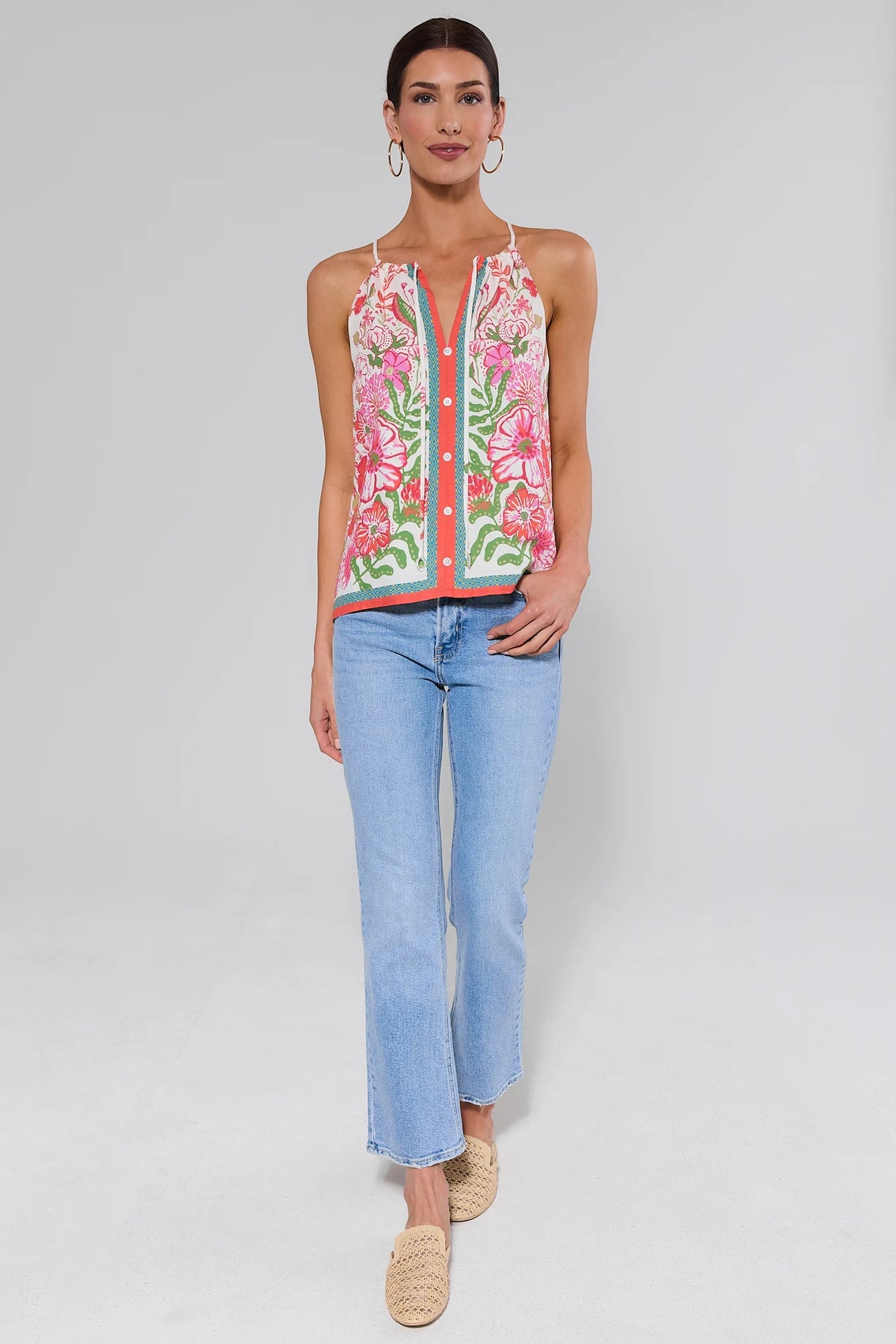 Woman wearing a colorful floral top and light blue jeans on a white background