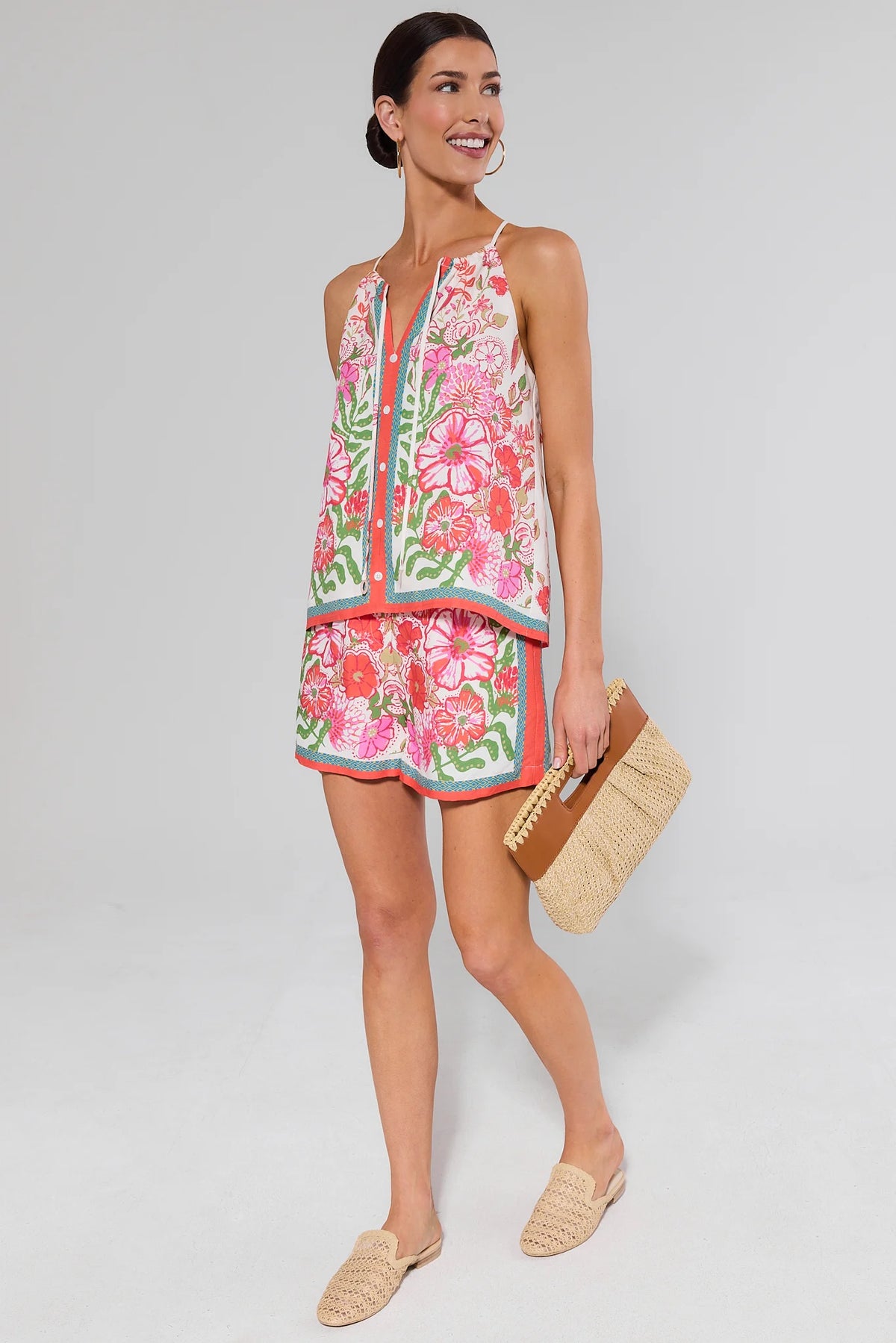 Woman wearing a colorful floral top and shorts and holding a straw bag on a white background