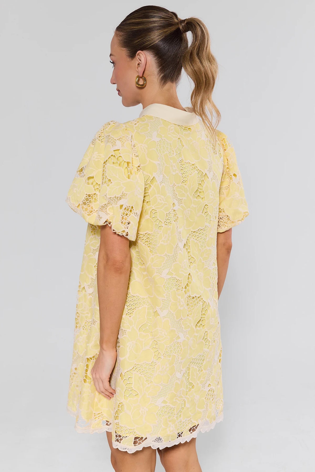 Woman standing wearing a yellow lace dress against a plain background