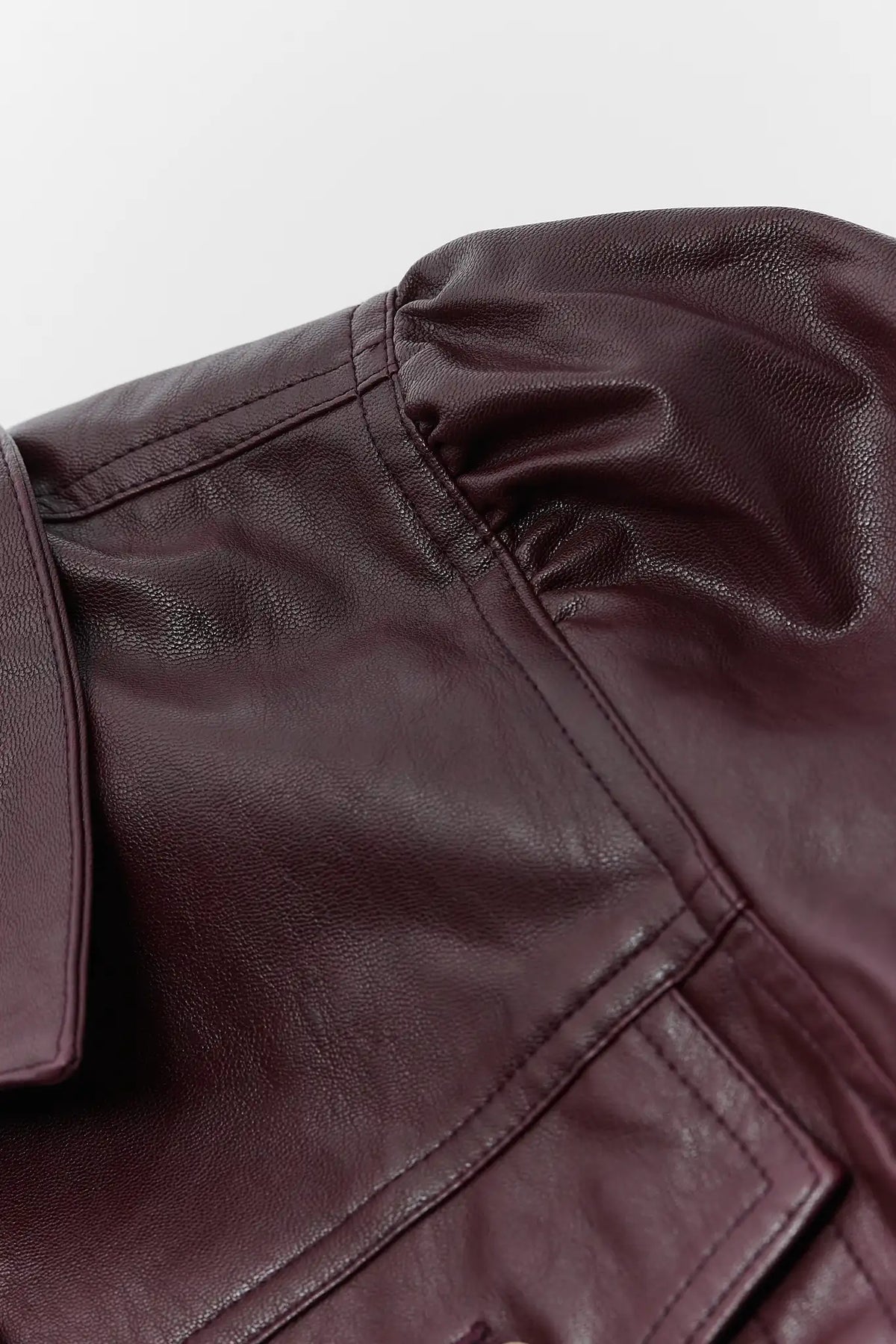 Brown faux leather jacket puff sleeve seam & fabric texture close-up on light background | Avara