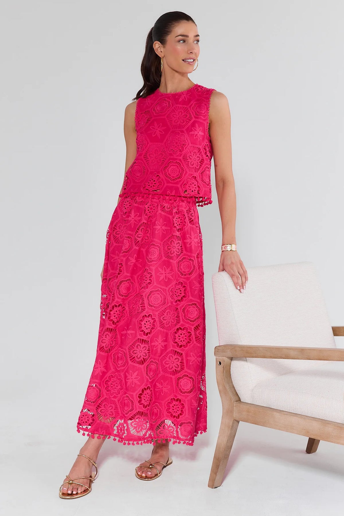 Woman models the Arden Pink Eyelet Top, a sleeveless cropped fuchsia lace piece with eyelet embroidery, paired with a matching scalloped ankle-length skirt.