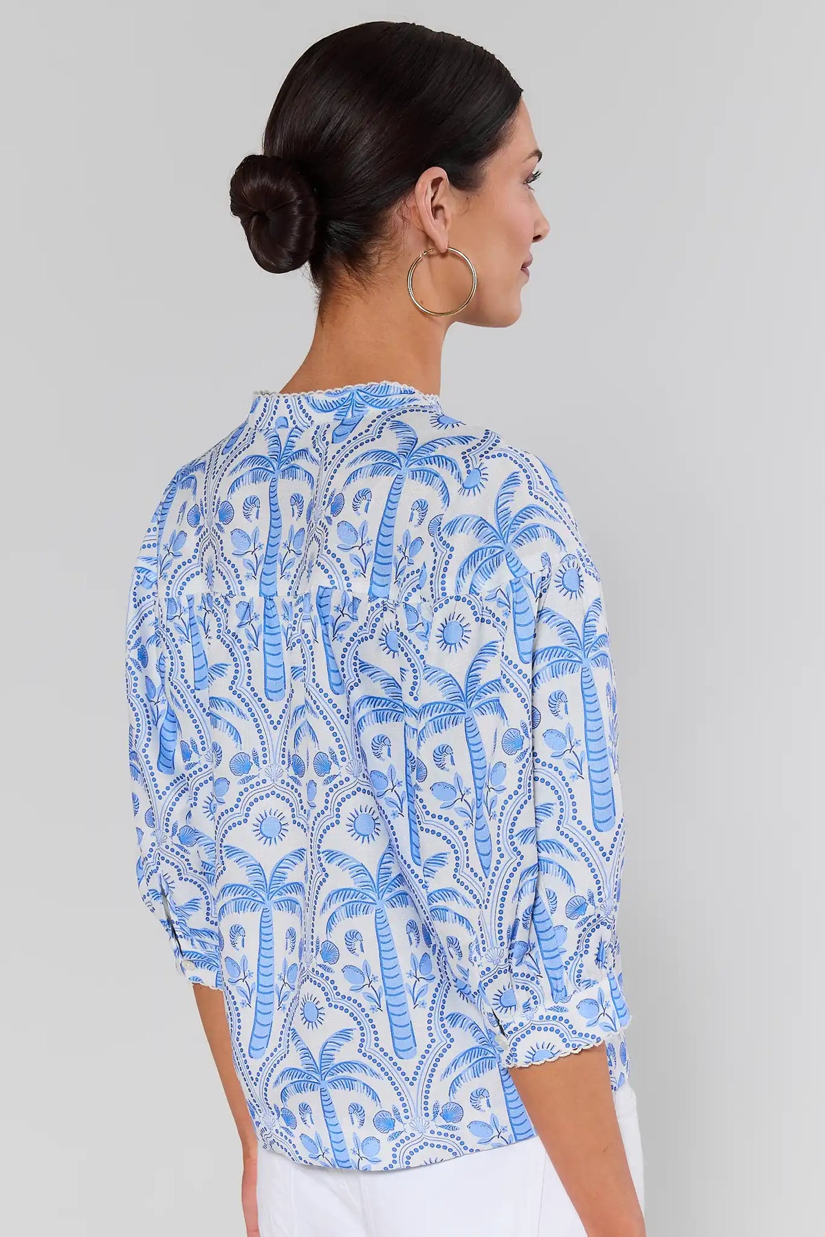 Woman standing wearing a blue and white patterned blouse against a gray background