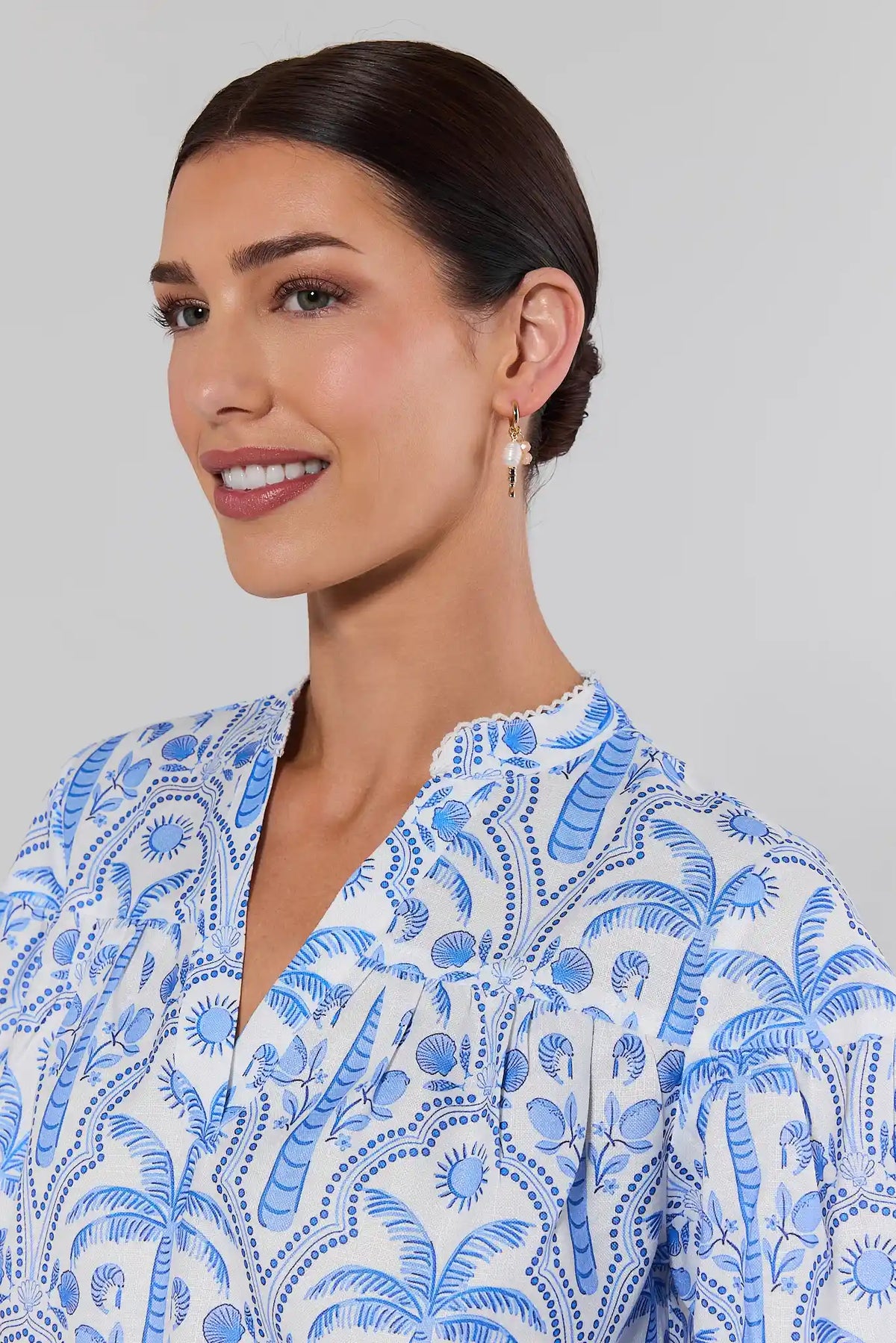 close up Woman wearing a blue and white patterned blouse with pearl earrings against a gray background