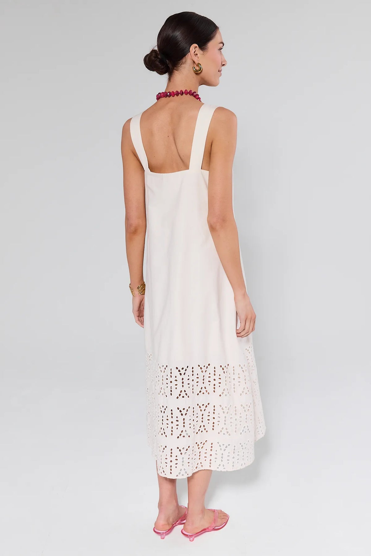 Woman in Melody Bone Eyelet Midi Dress, featuring a square neckline and eyelet hem, styled with pink accessories and gold jewelry, creating a chic, minimalist look.