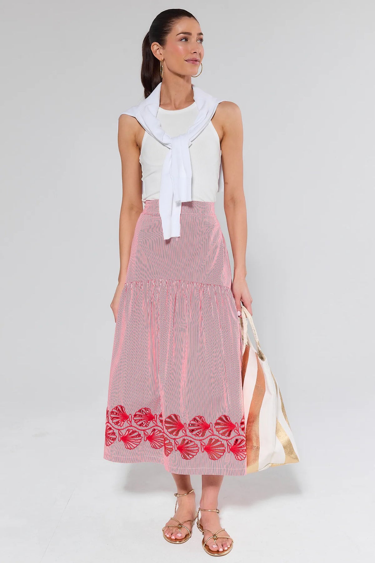 Woman wearing a white sleeveless top and red patterned skirt on a plain background
