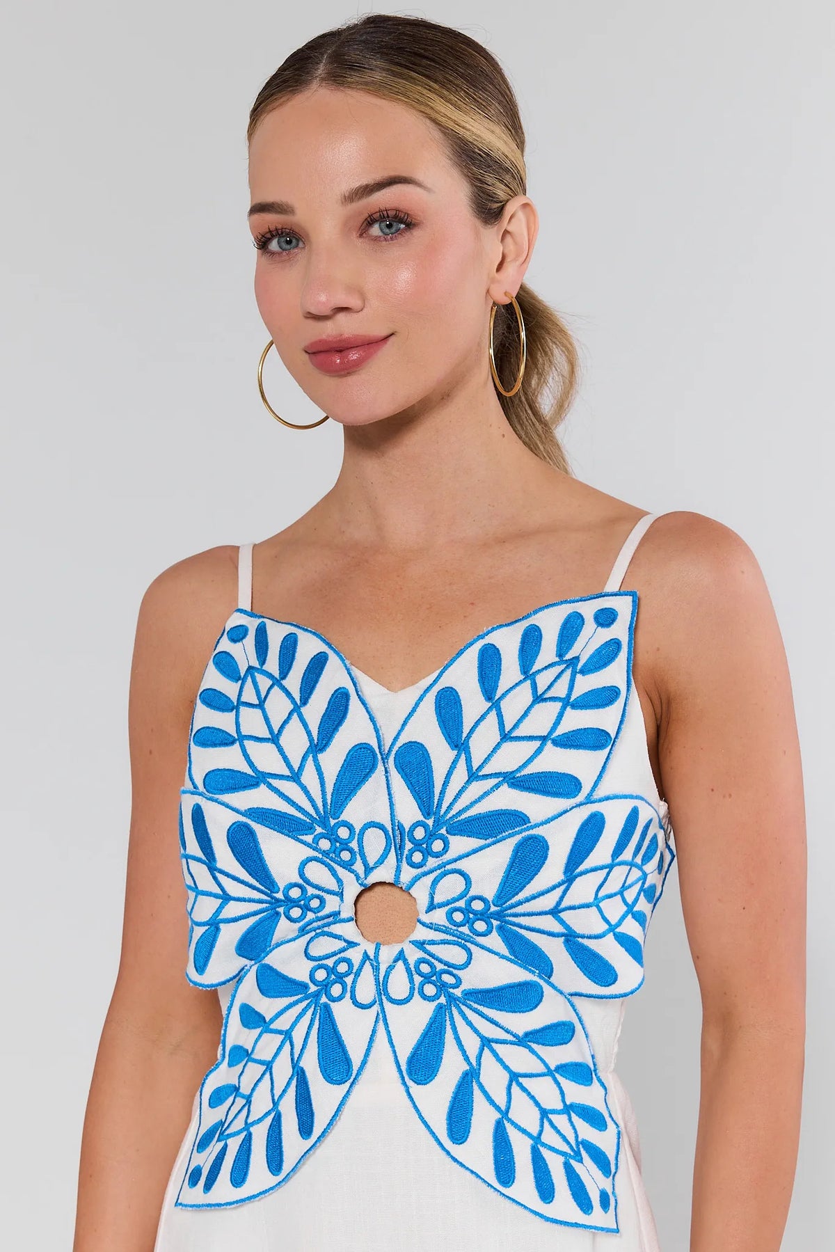 Woman wearing a white top with blue floral patterns on a plain background
