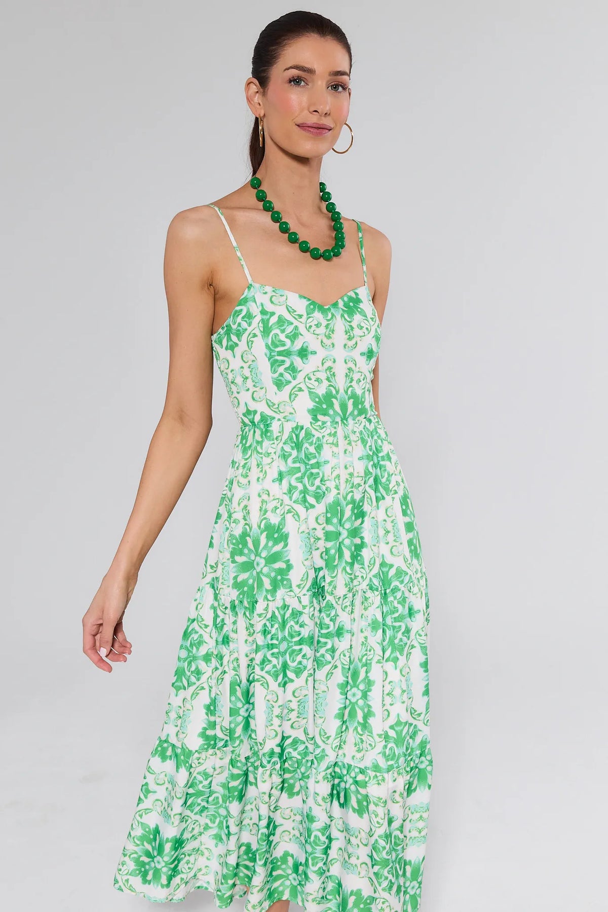 Model in the Lori Green Printed Midi Dress, featuring a fitted bodice, sweetheart neckline, tiered skirt, accessorized with gold hoops and green necklace.