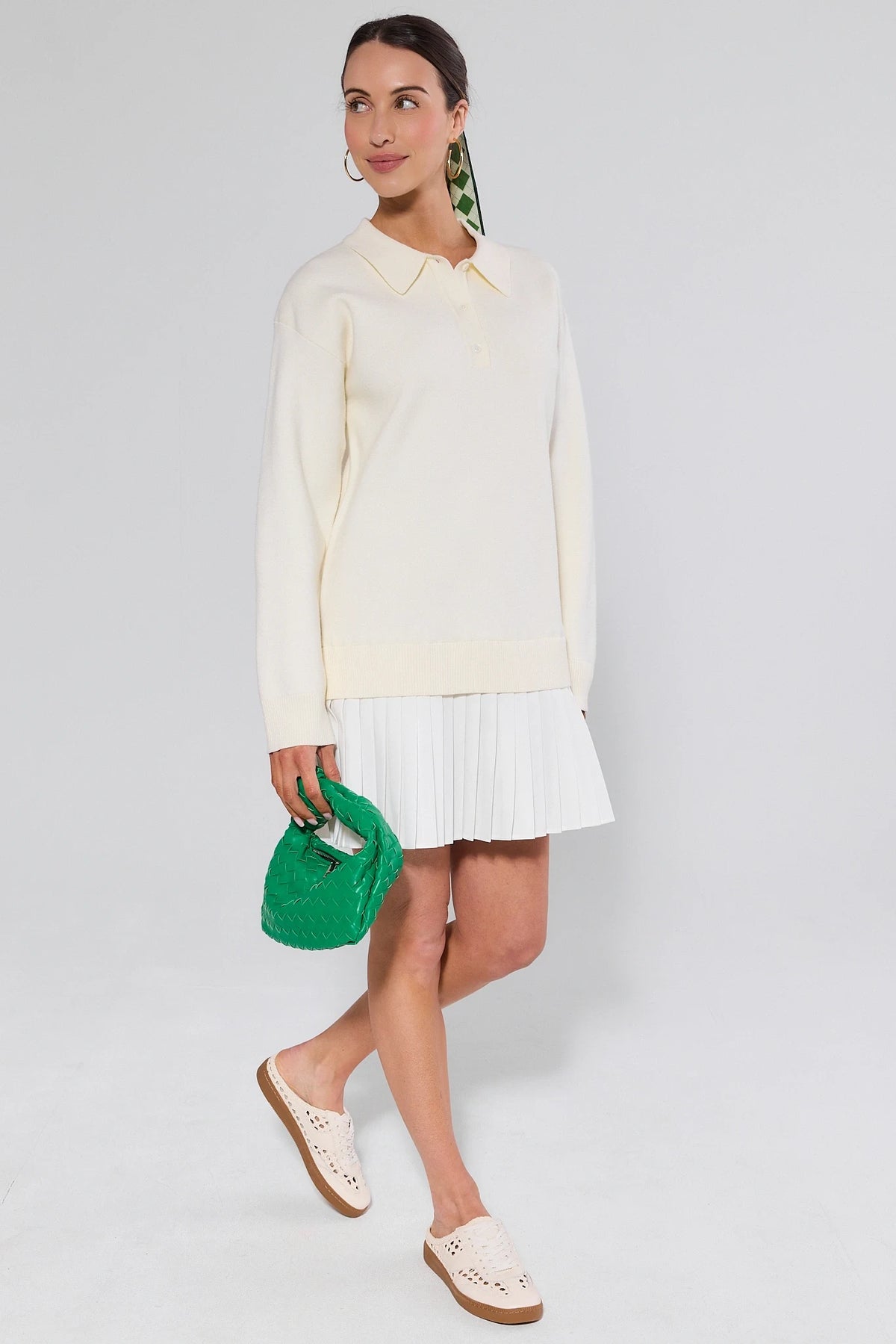 Woman wearing a light-colored blouse and white skirt, holding a green clutch against a plain background