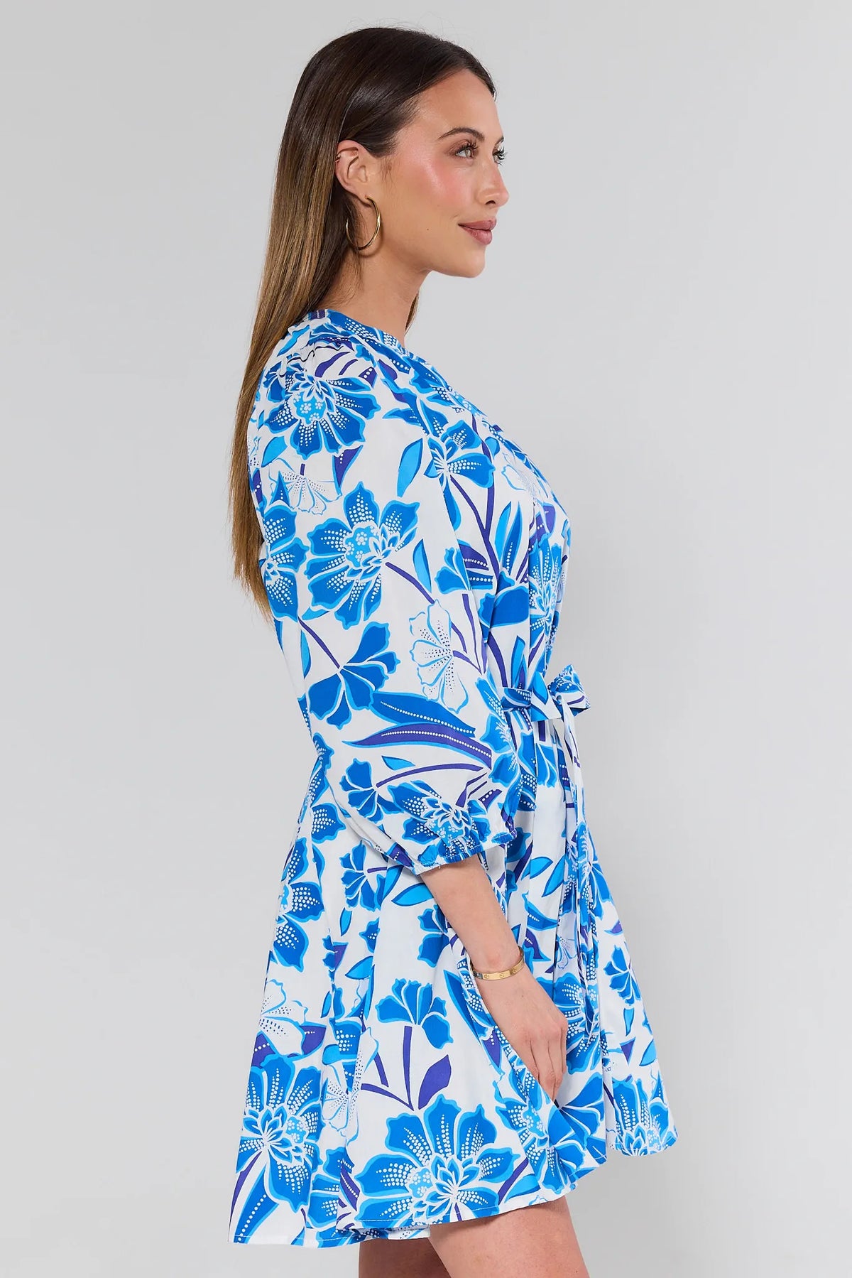 Woman wearing blue floral mini dress showing tie waist and flowy skirt - Side Profile | Avara