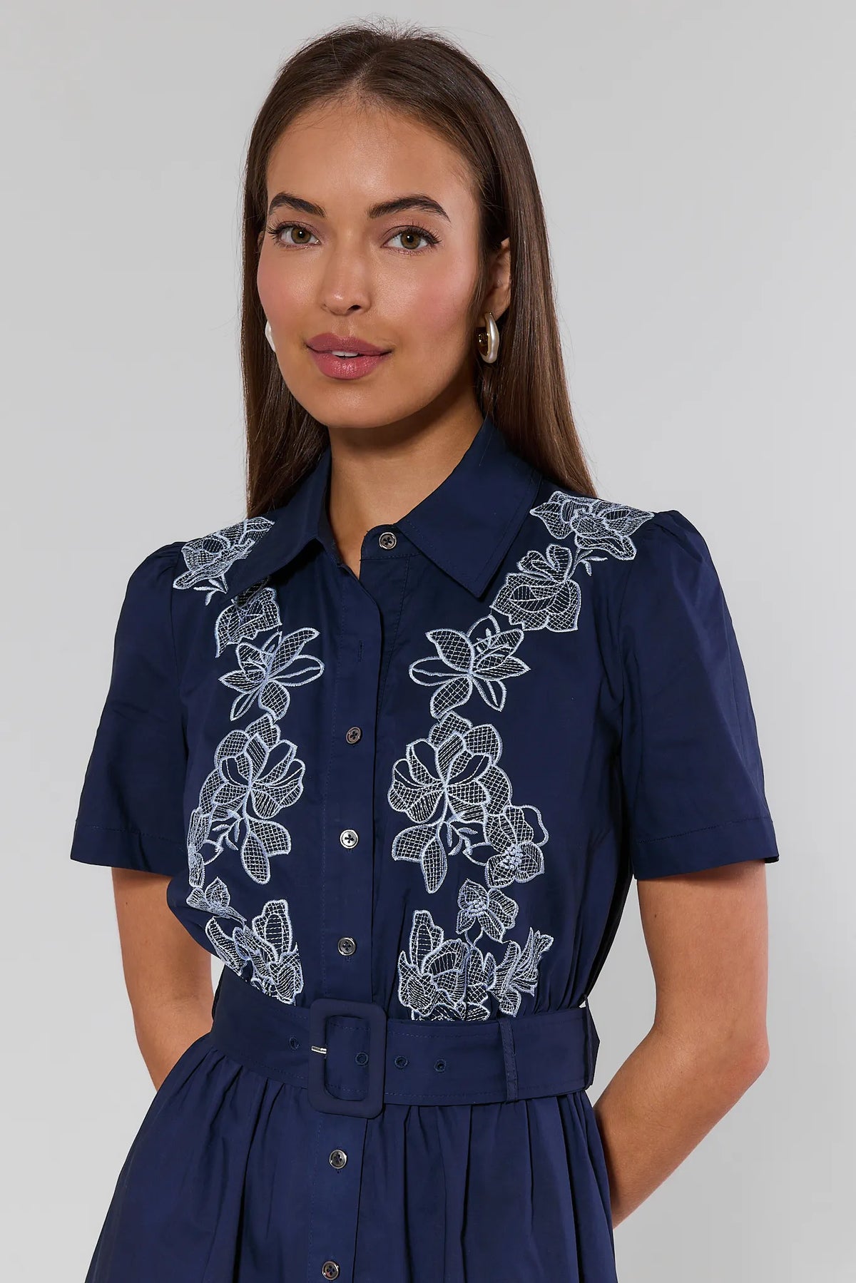 Close-up of navy embroidered dress with white floral lace bodice detail, collar neckline, and belted waist | Avara