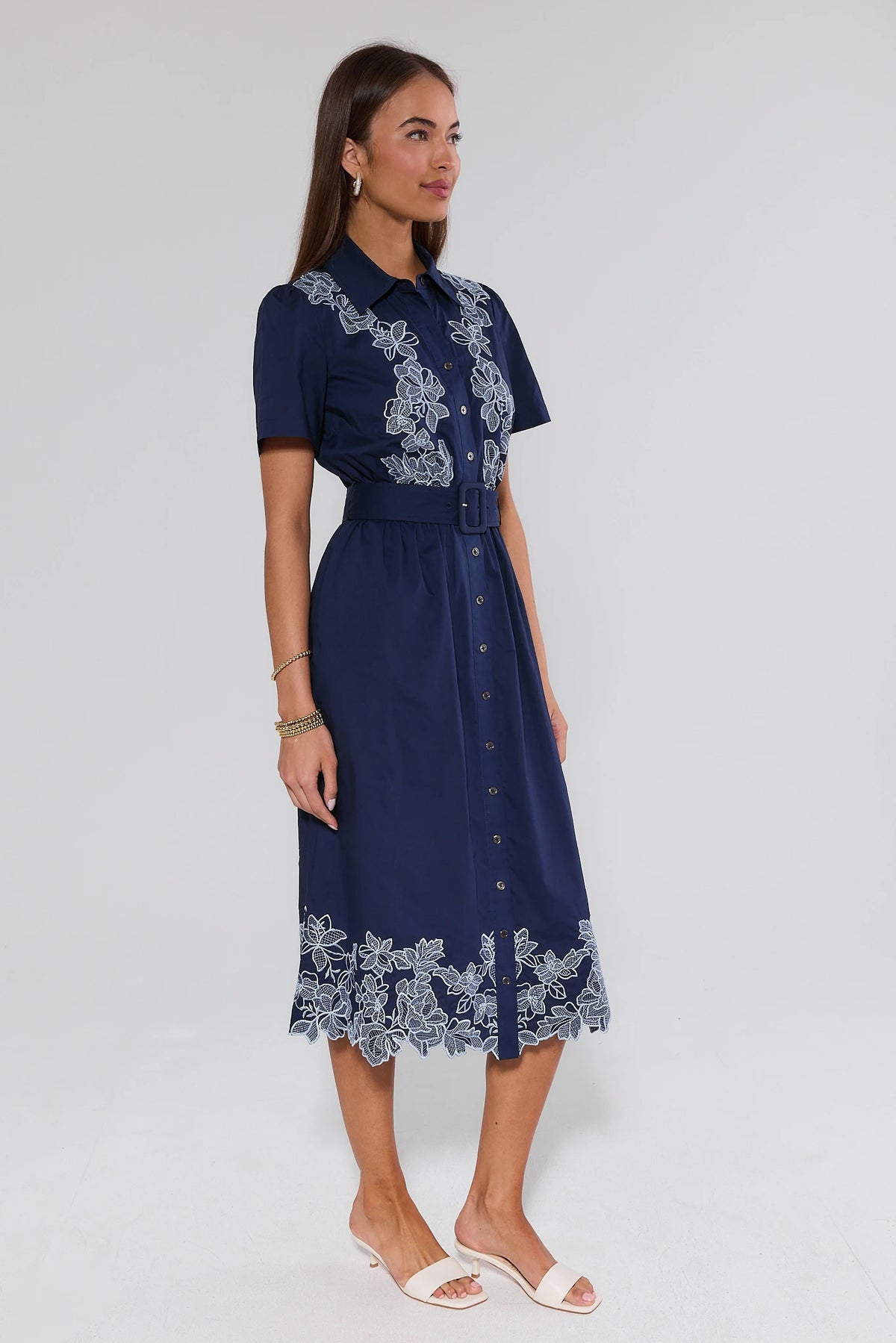 Back view of navy embroidered midi dress showing belted waist and white floral lace scalloped hem detail | Avara