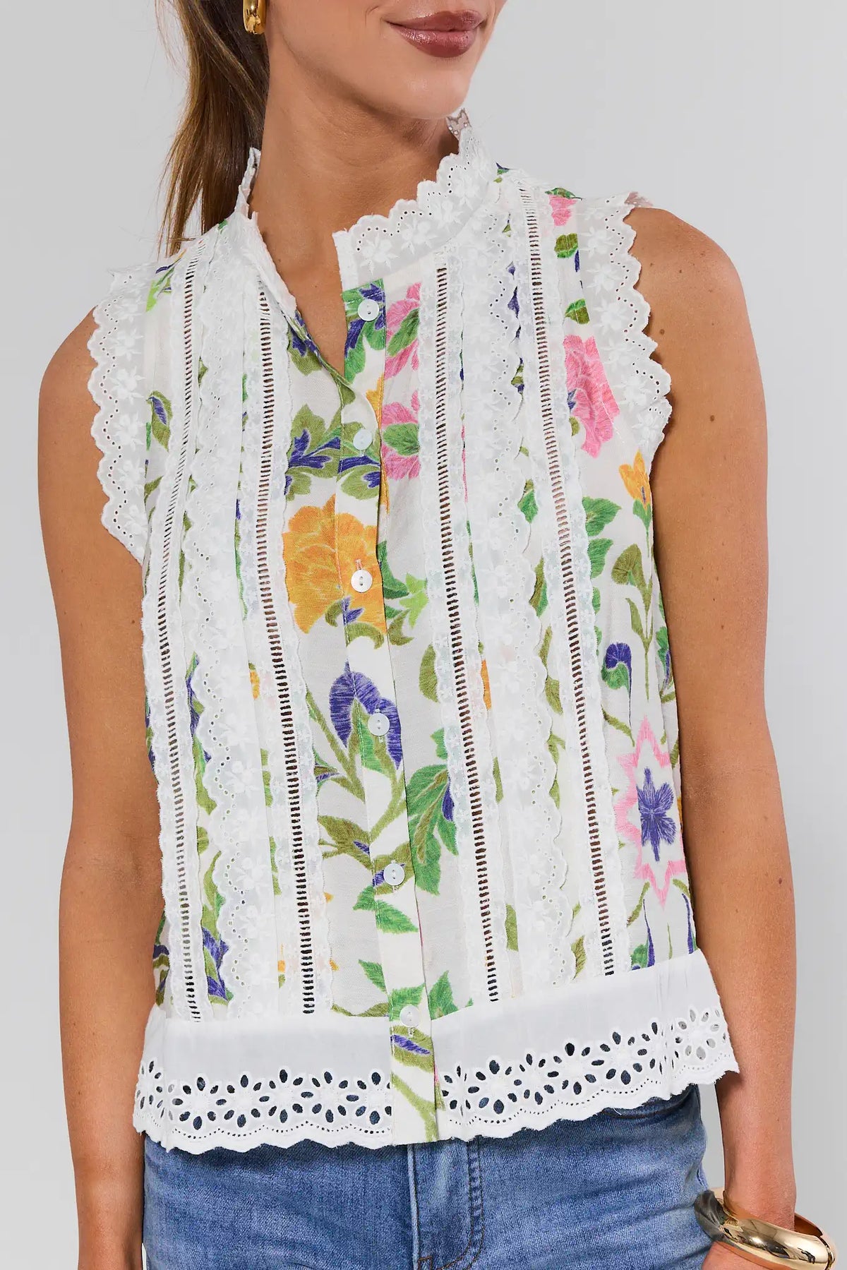 Woman wearing a sleeveless floral top with lace details on a plain background