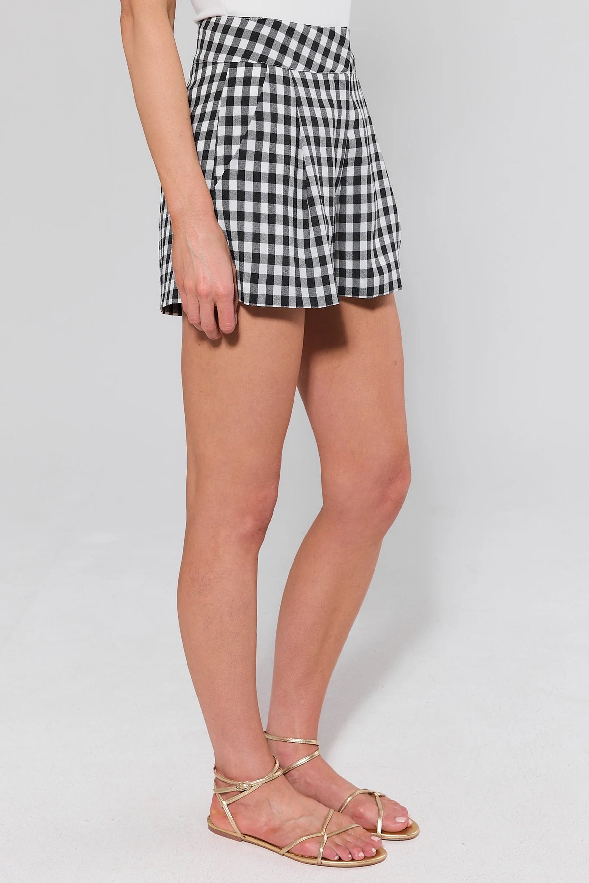 Black and white gingham tailored shorts, side view showing pleated silhouette and gold sandals | Avara