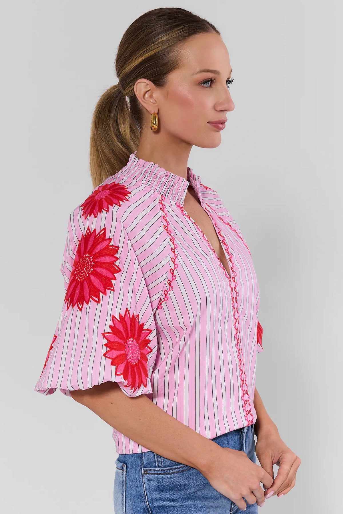 Side view of pink striped blouse with bold red floral embroidery on puff sleeves, styled with denim | Avara