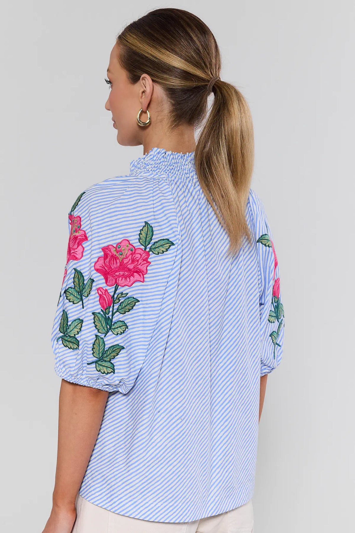 Woman wearing blue striped floral embroidered top showing smocked neckline and rose sleeve detail - Back View | Avara
