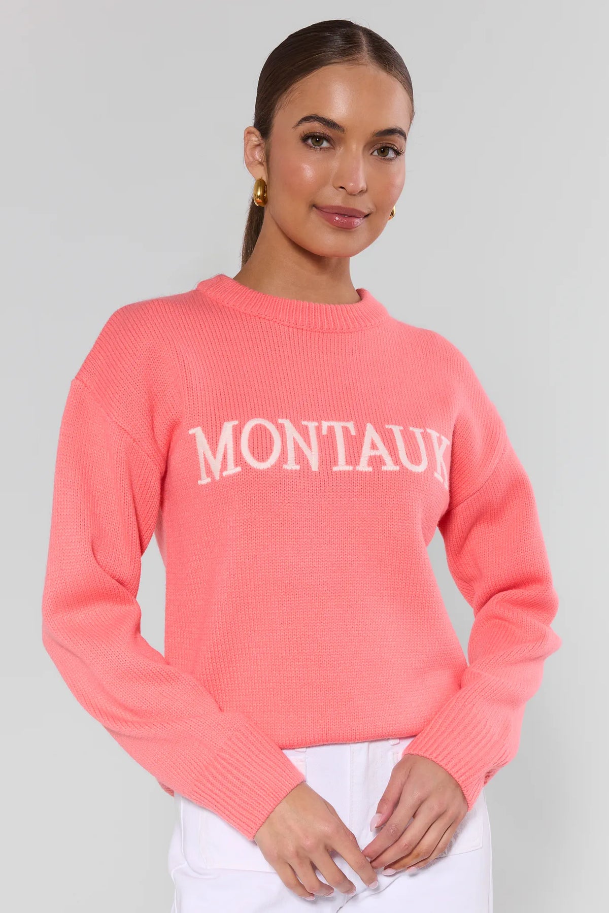 Coral knit sweater with 'Montauk' contrast lettering, crew neck, front three-quarter view on model | Avara