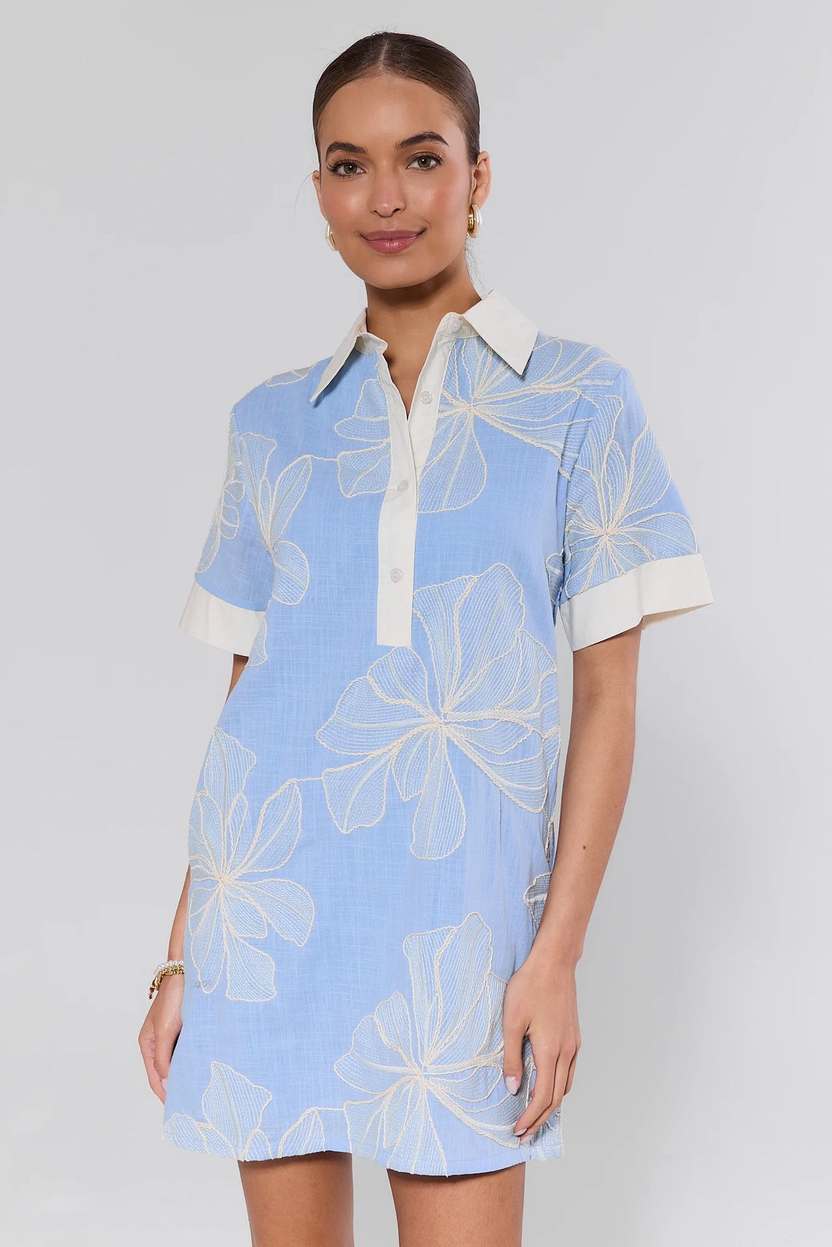 Woman wearing a light blue dress with white floral patterns on a plain background