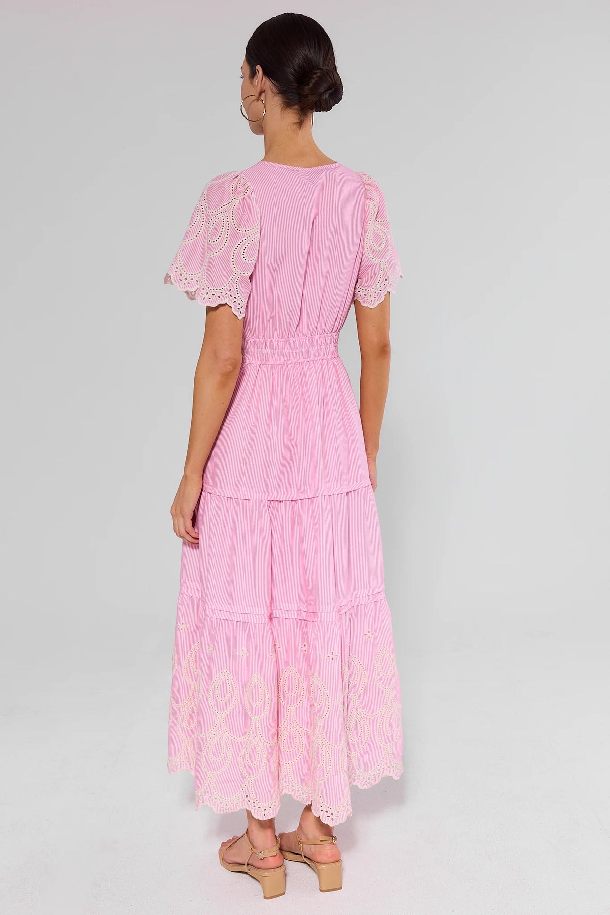 Woman standing wearing a pink dress with lace details on a gray background