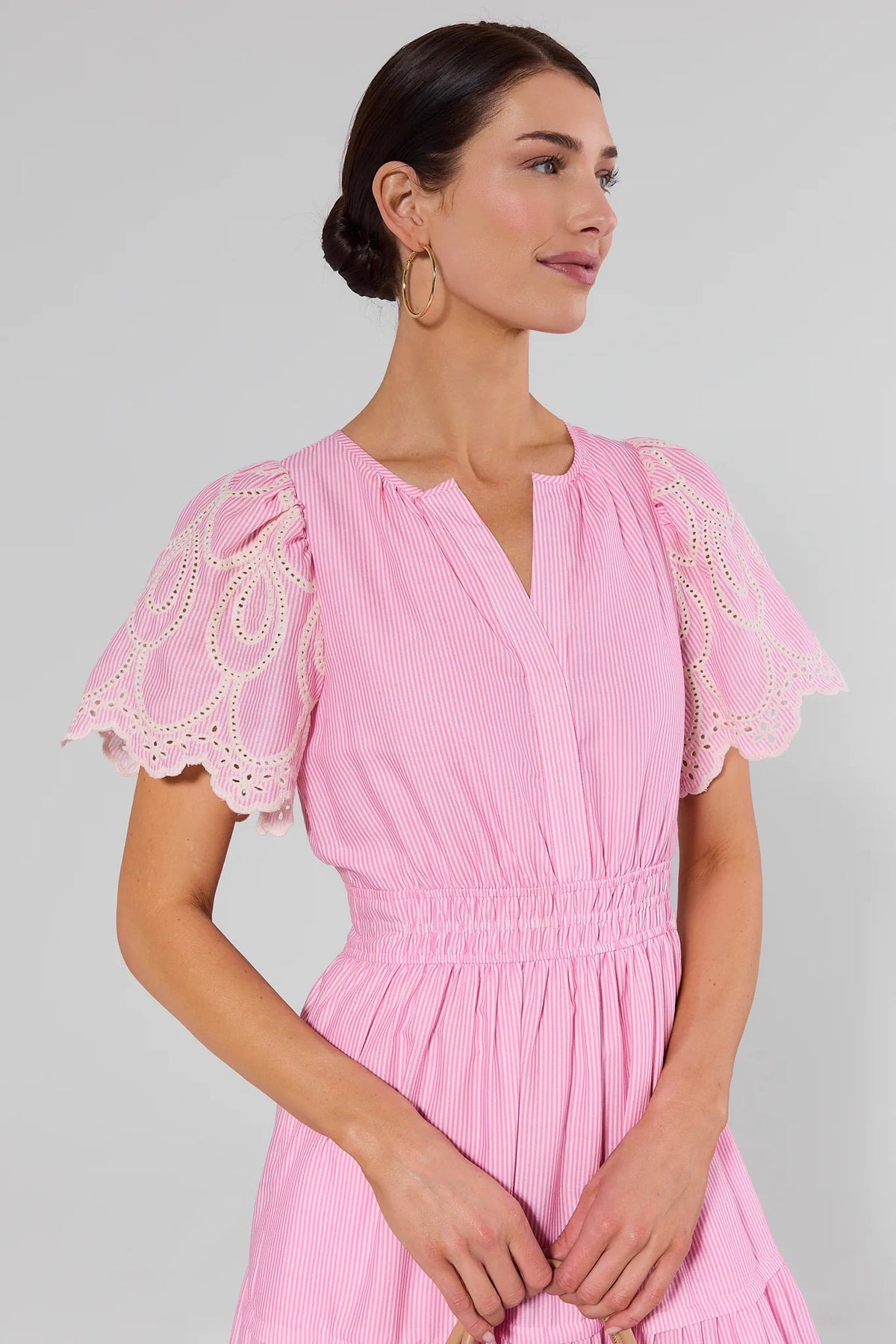 Woman wearing a pink dress with lace sleeves on a gray background