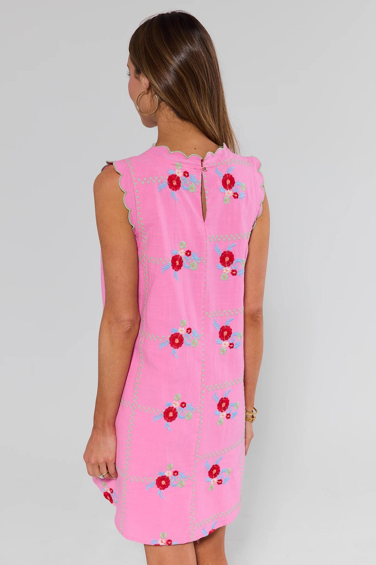Woman standing wearing a pink dress with floral patterns on a plain background