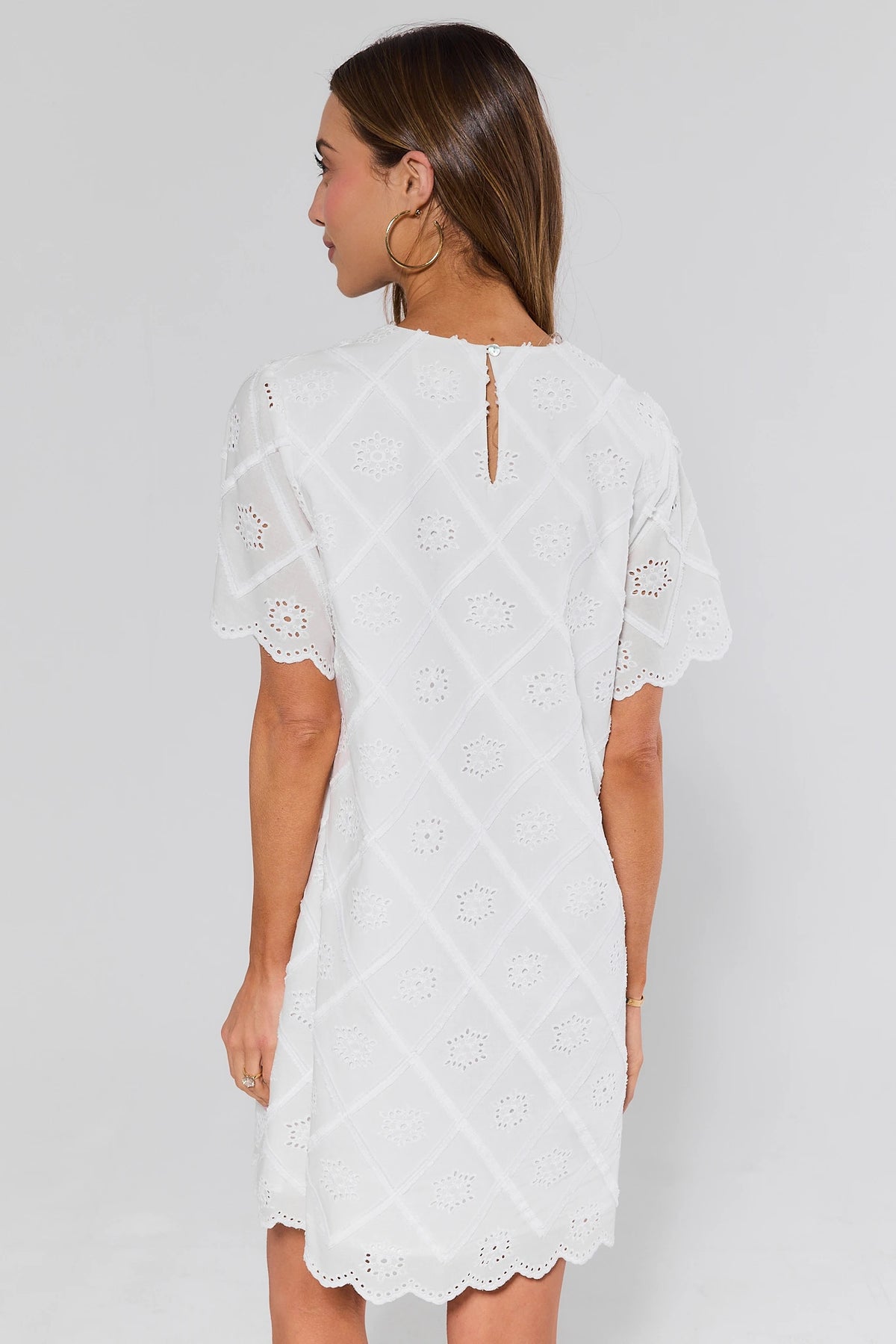 Woman standing wearing a white lace dress against a plain background