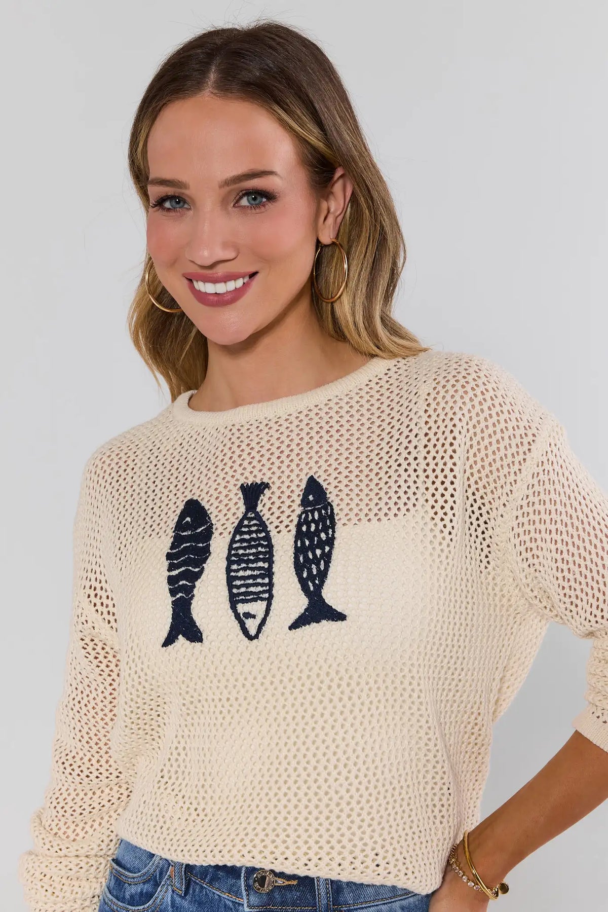 close up Woman wearing a beige sweater with fish designs on a plain background